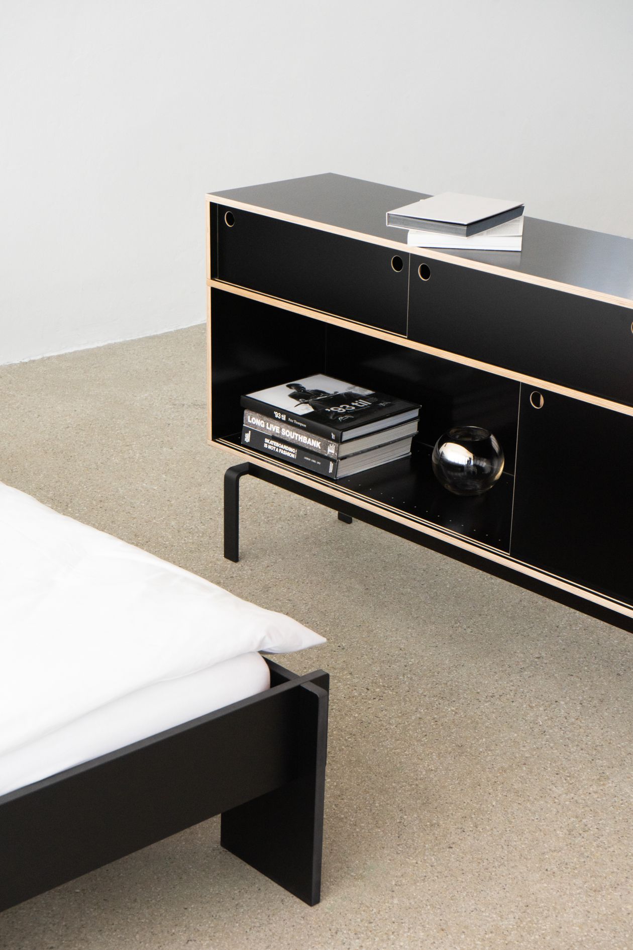 Schwarzes Egal Sideboard von Nils Holger Moormann mit Büchern und Deko-Objekt im minimalistischen Schlafzimmer.