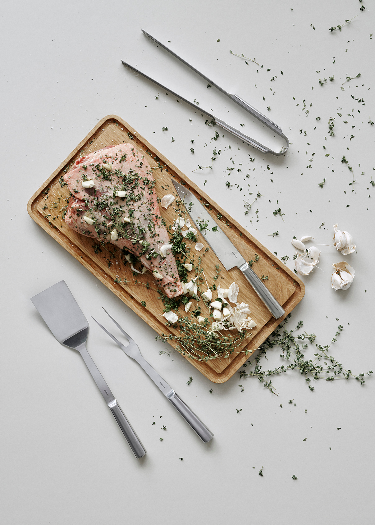 Produktfoto: Sixtus Grillzange und Grillbesteck neben mariniertem Fleisch auf Holzbrett.