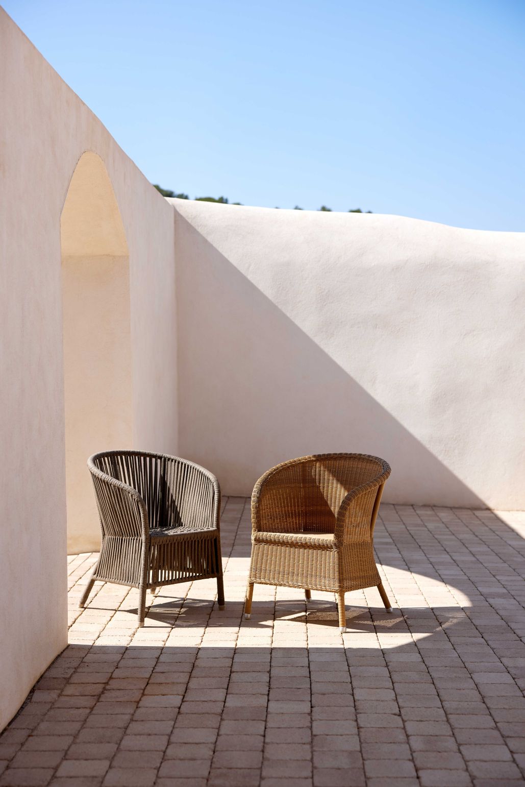 Derby Outdoor Stuhl / Sessel von Cane-Line in Taupe und Natur vor weißer Mauer.