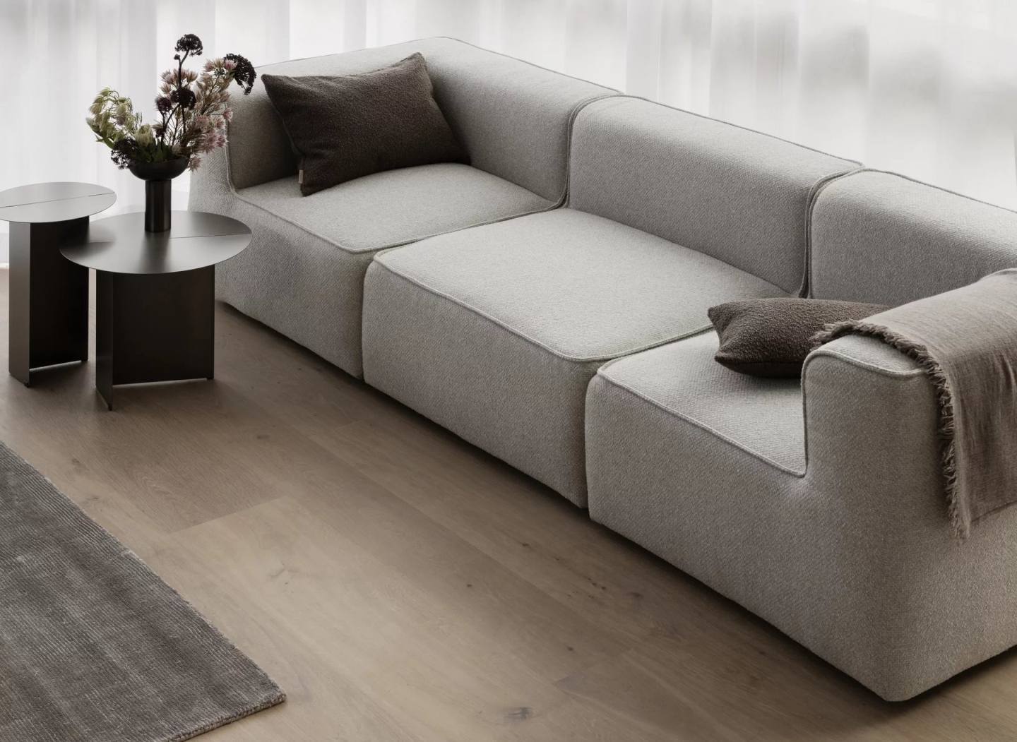 Oru Beistelltisch von Blomus, Ø 50 cm, neben einem grauen Sofa mit Kissen.