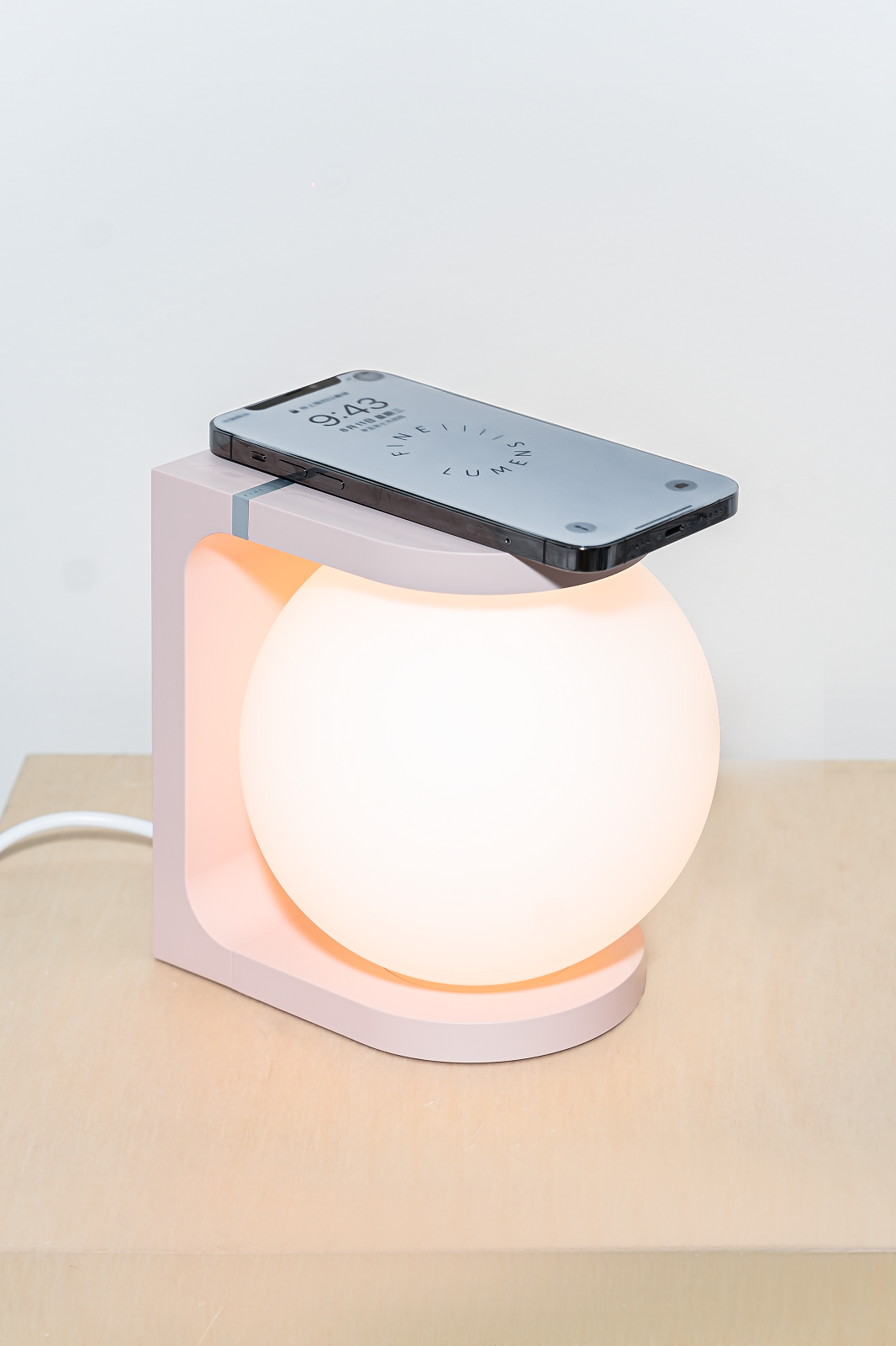 Plat Reading Lamp Tischleuchte: Rosa Nachttischlampe mit Globus-Design und Smartphone auf der Ladefläche.