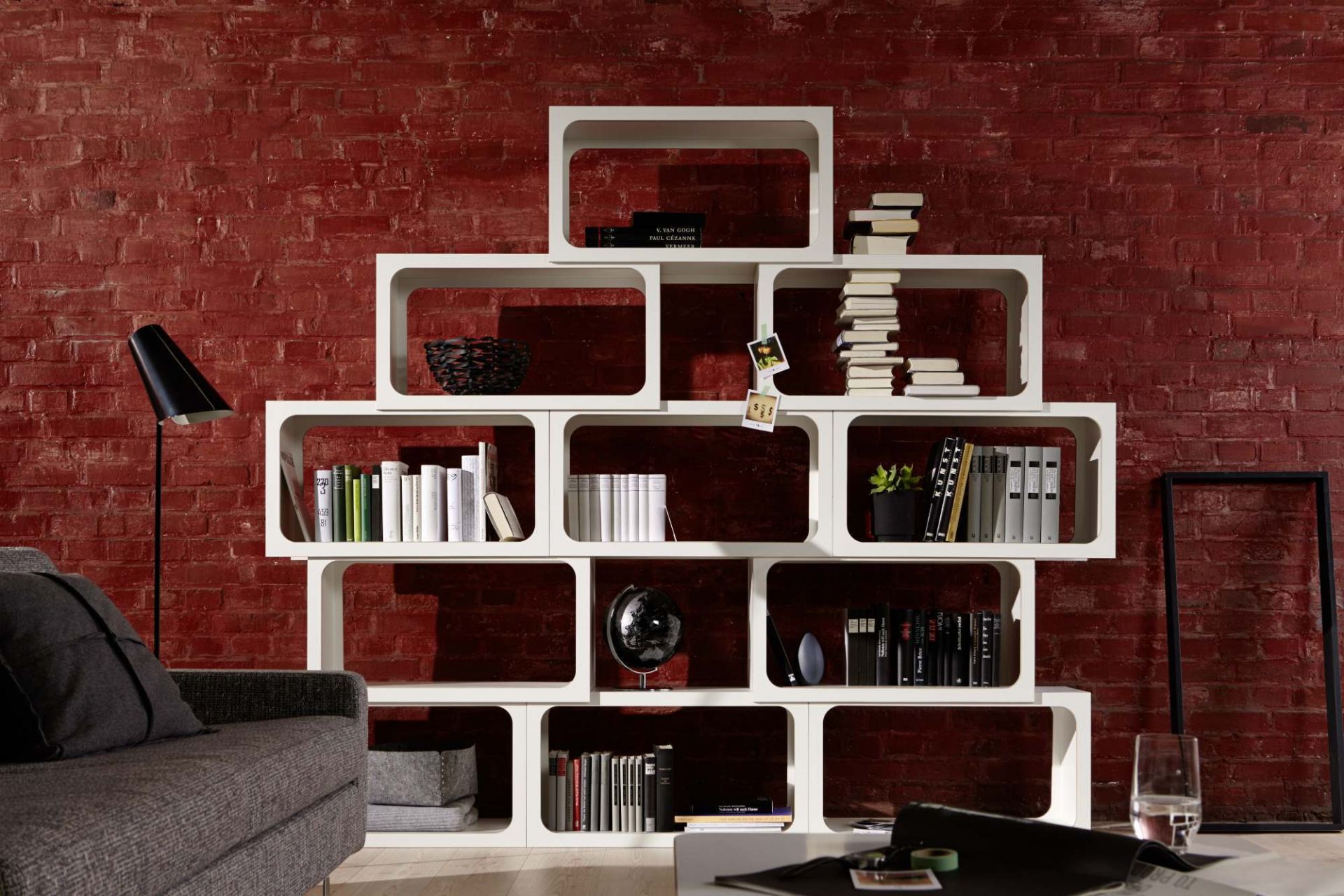 Weißes modulares Regal vor roter Backsteinwand, gefüllt mit Büchern und Dekoration, modernes Wohnzimmer Design.
