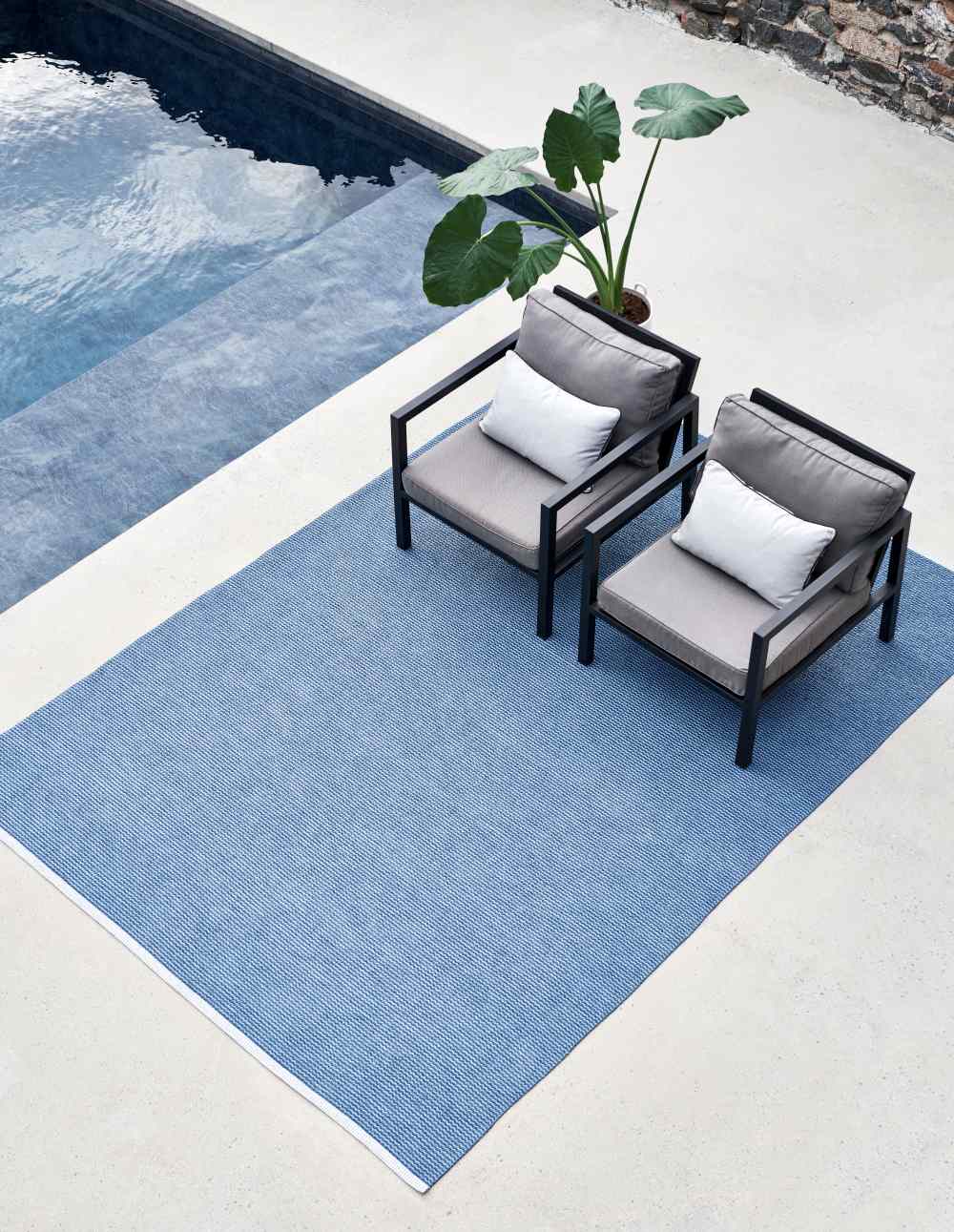 Blauer Kunststoffteppich von Pappelina (ca. 230x320 cm) im Außenbereich mit zwei Stühlen und Pflanze.