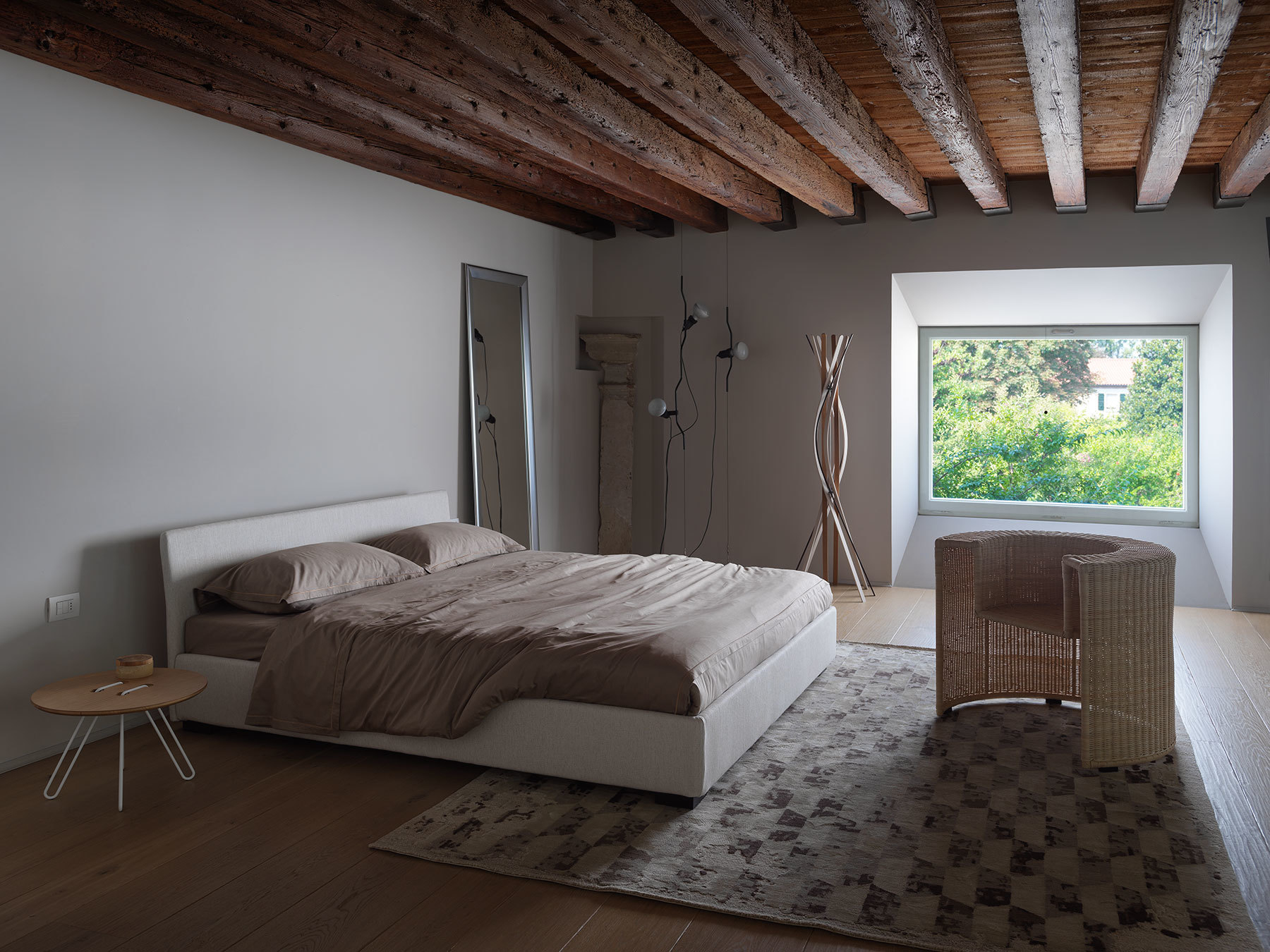 Schlafzimmer mit Casamania Horm Twist Garderobenständer aus Buchenholz, neben Bett und Rattansessel.