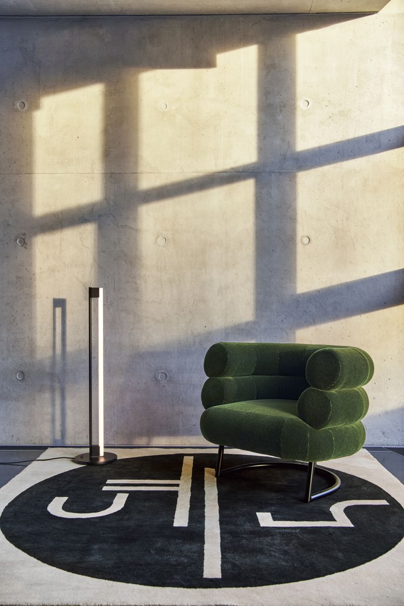 Moderne Tube Light Stehleuchte in Schwarz von ClassiCon neben grünem Sessel und gemustertem Teppich.