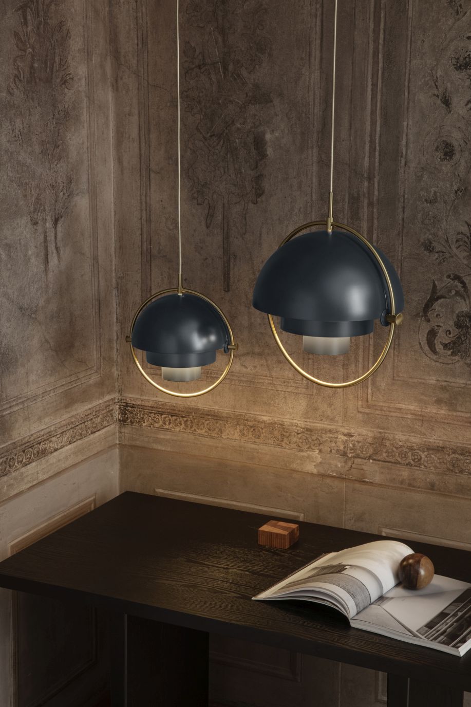 Zwei Gubi Multi-Lite Pendelleuchten in Chrom über einem dunklen Tisch mit Buch.