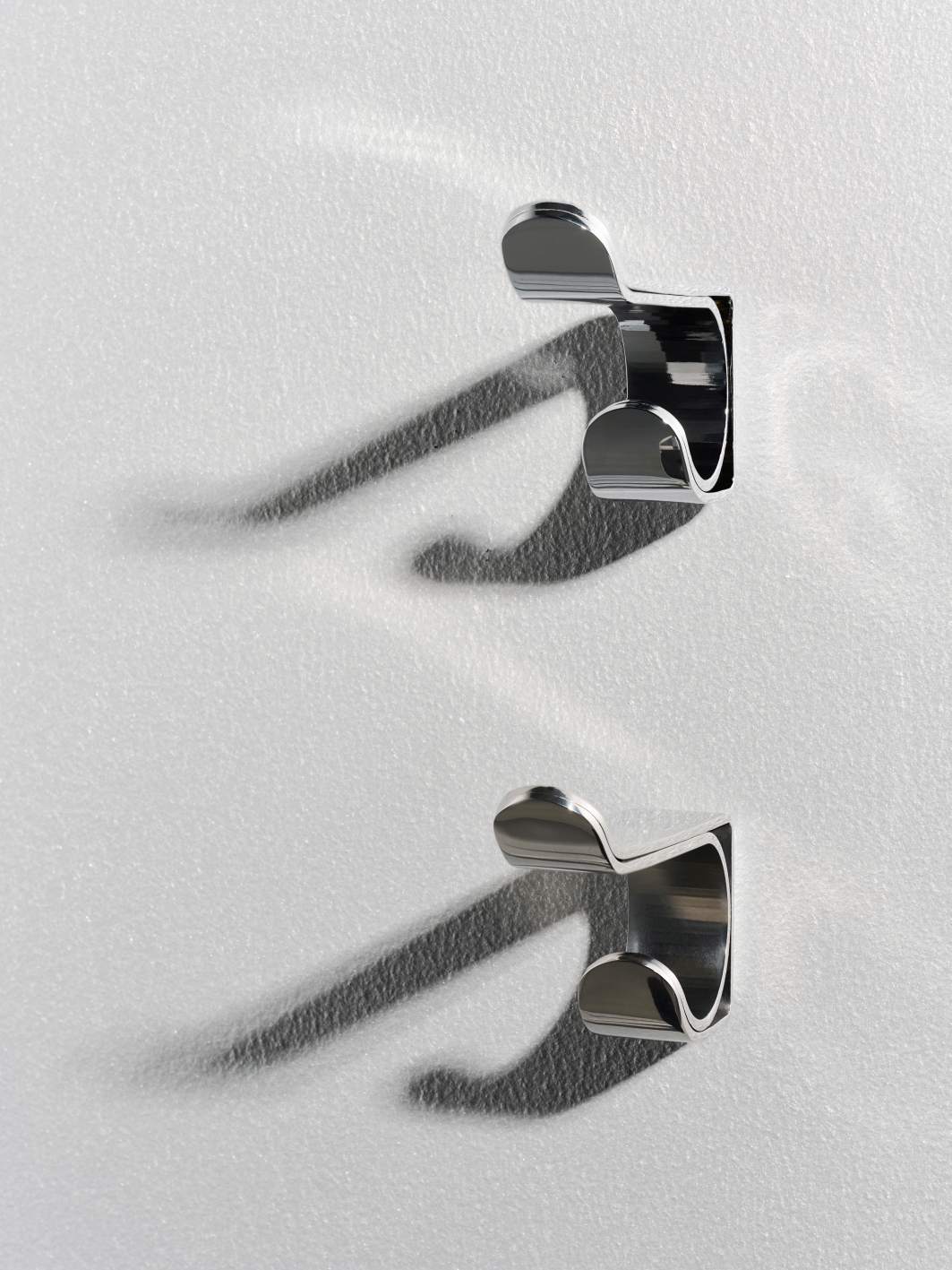 Zwei silberne Ayla Wandhaken von Schönbuch an einer weißen Wand. Design Haken.