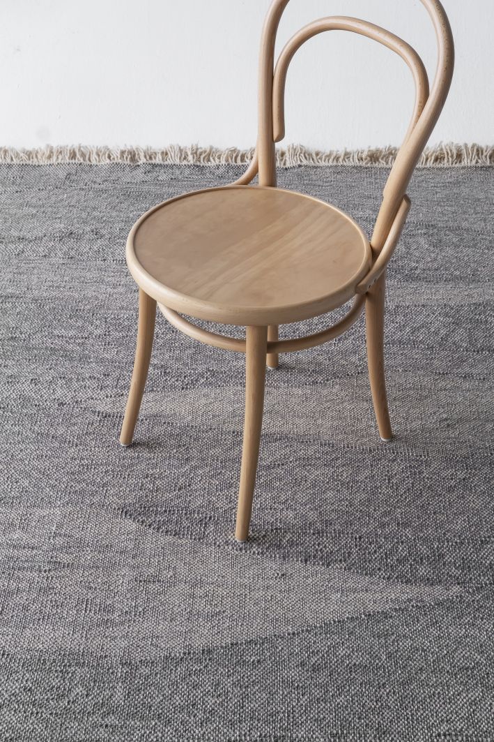 Telares Teppich Pine von Nanimarquina, grauer Wollteppich mit Fransen und Holzstuhl im Detail.