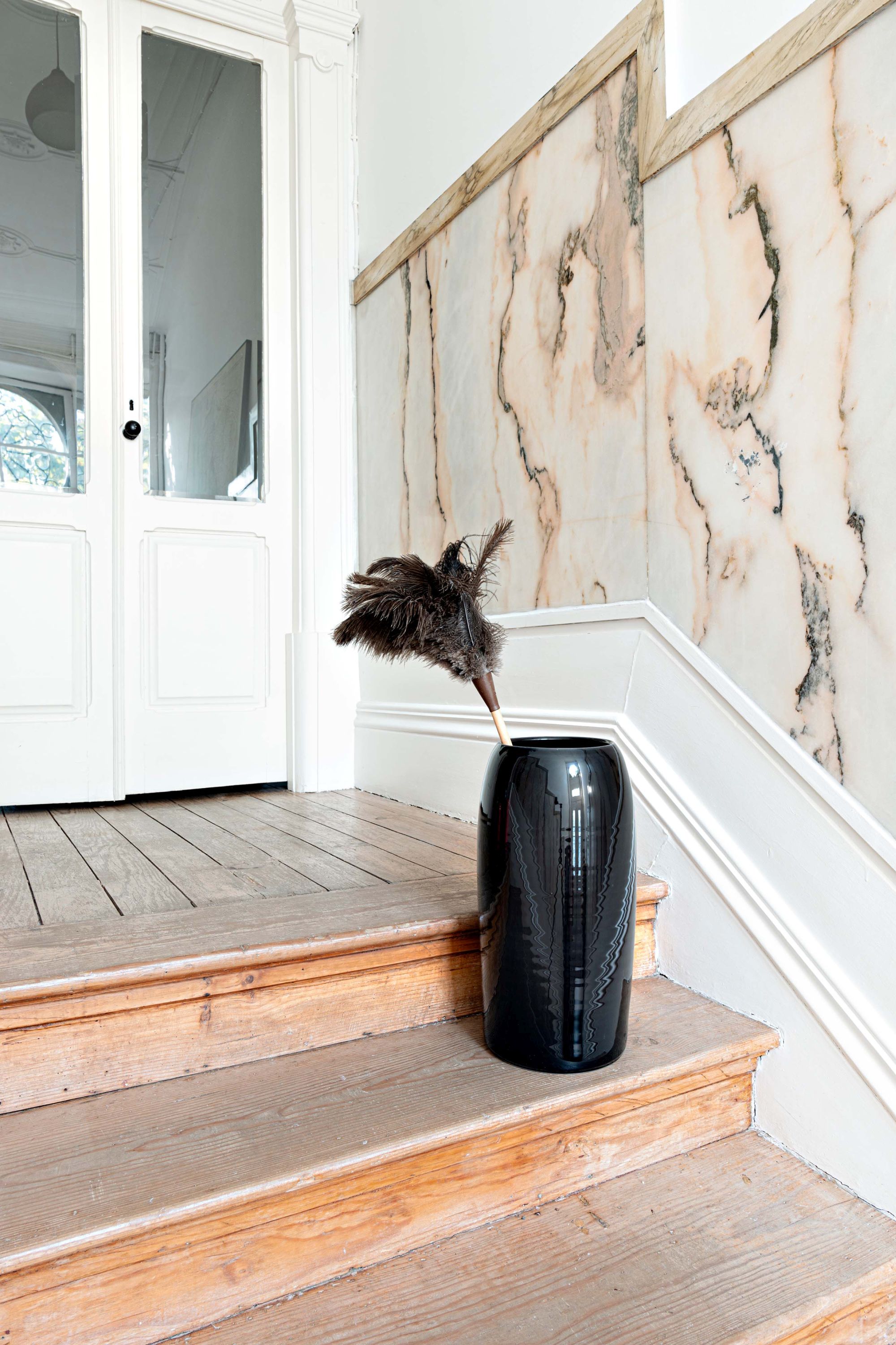 Carlo Schirmständer Charcoal Schönbuch: Schwarzer, zylindrischer Schirmständer mit Federbesen auf Holztreppe im Flur.