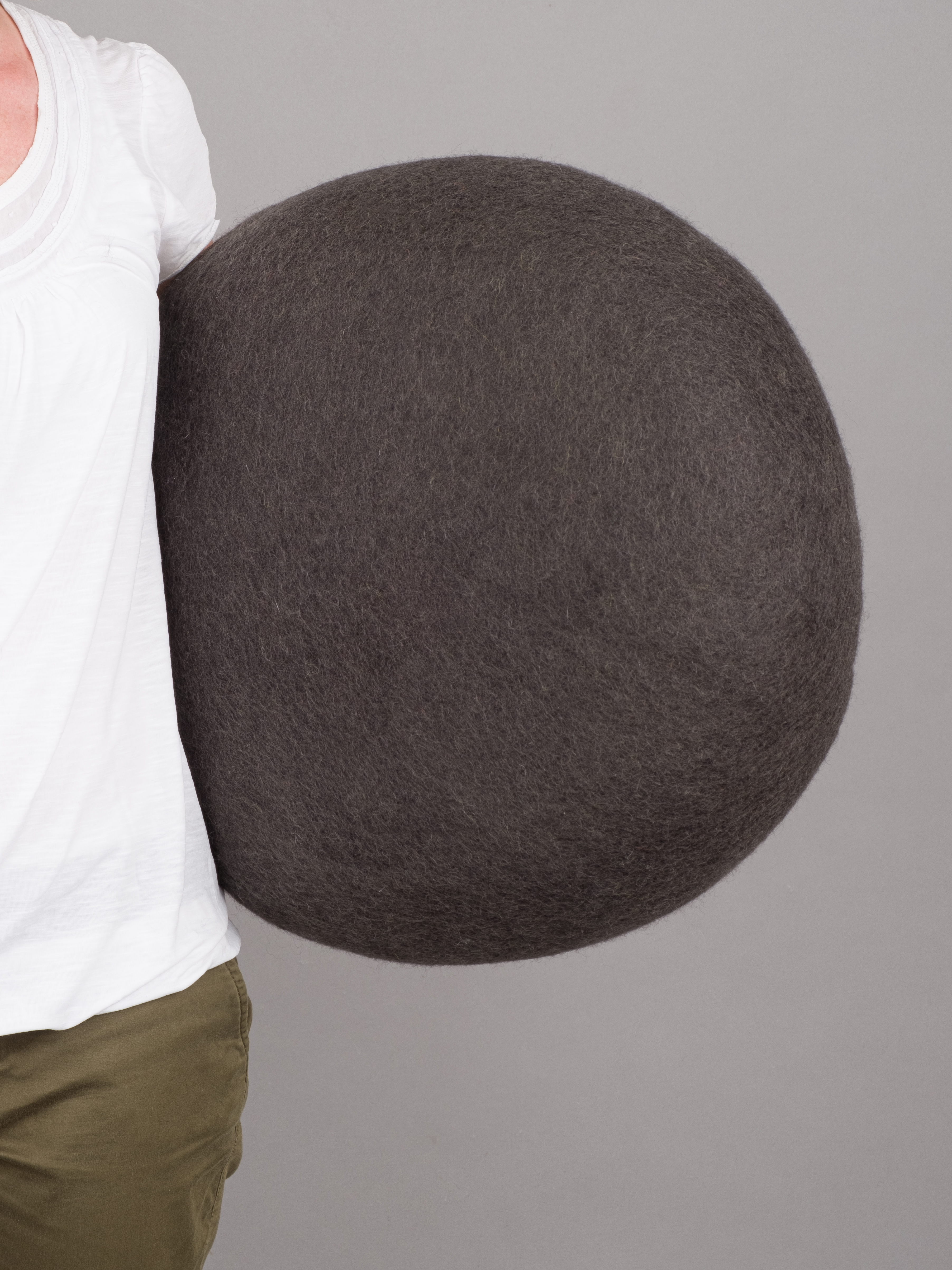 Grauer Filz Pouf Hocker von myfelt, Modell Kuno, wird von einer Person gehalten.