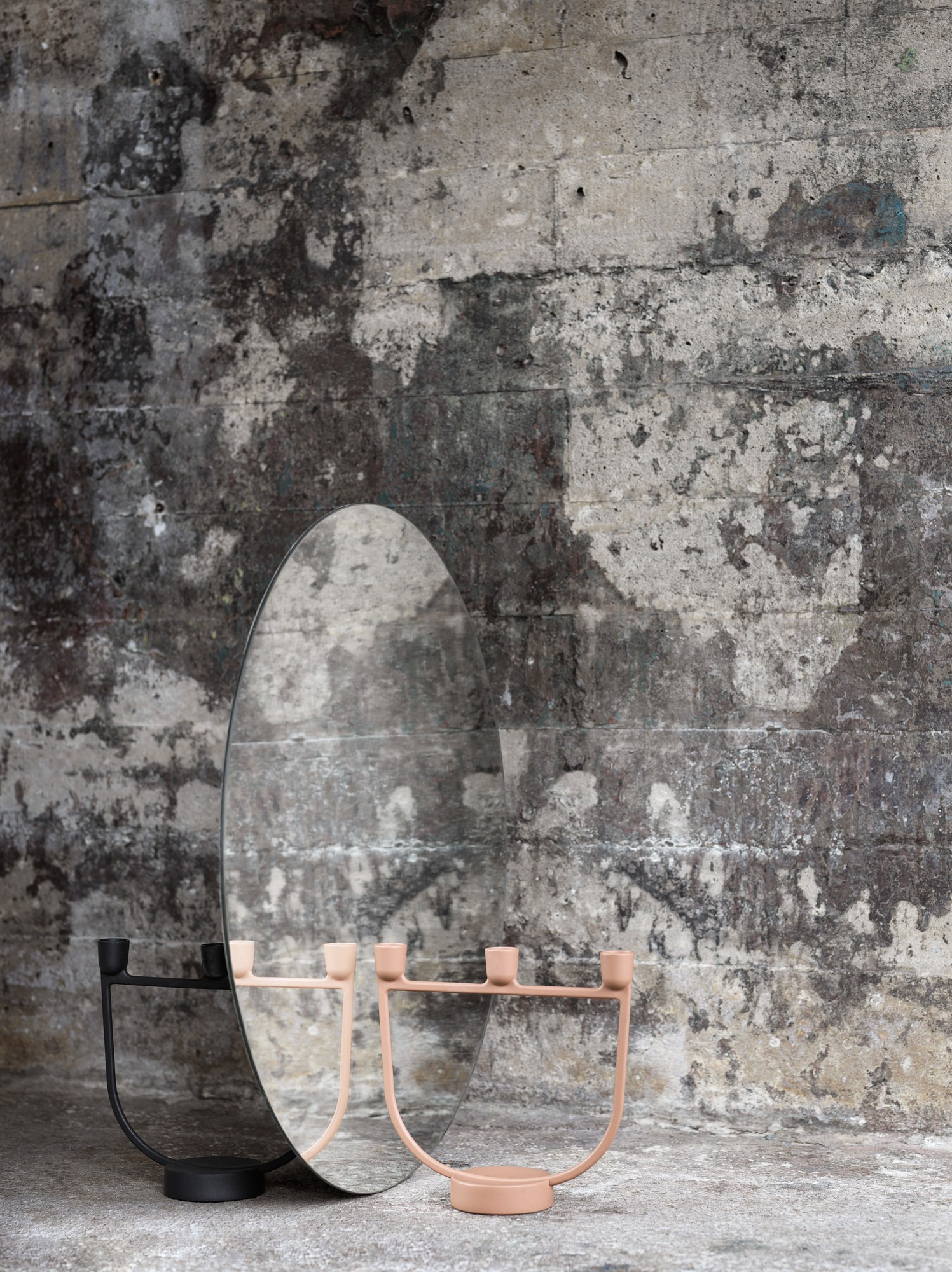 Muuto Open Candelabra Kerzenhalter in Schwarz und Rosa vor einem Spiegel und Betonwand.
