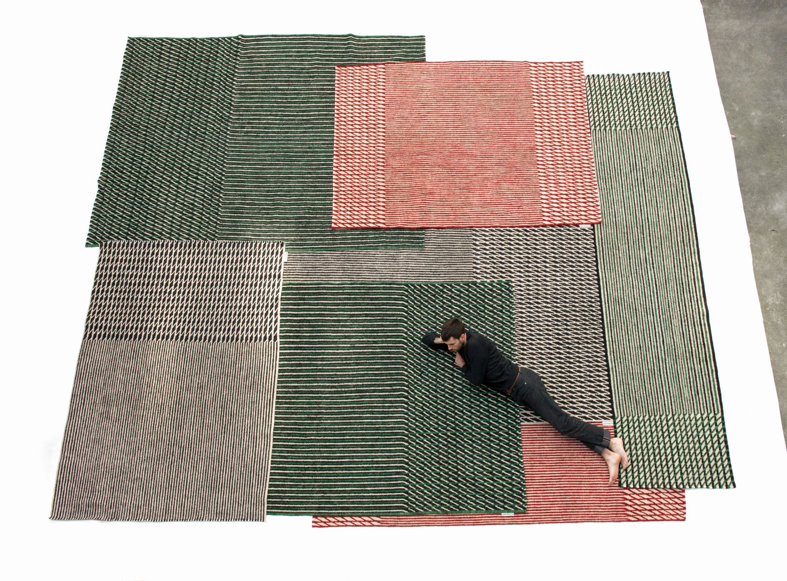 Mann liegt auf mehreren Nanimarquina Teppichen, Blur Läufer in Grün, Rot und Beige.