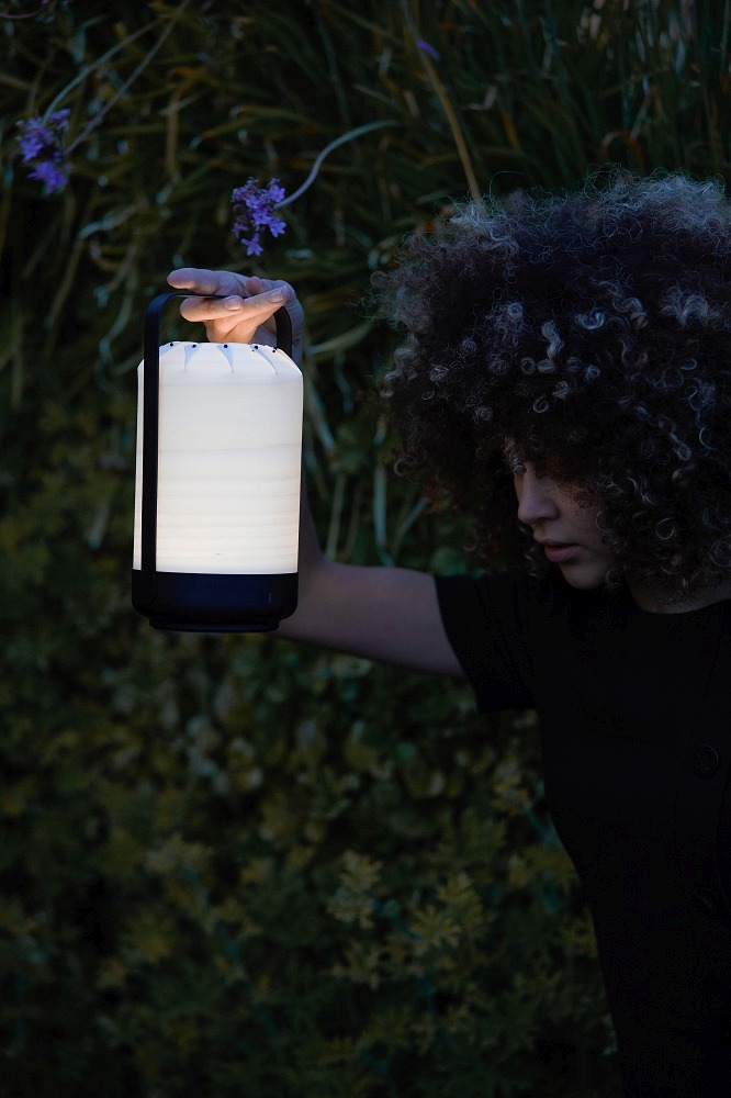 Frau hält Chou Mini LED Akkuleuchte von LZF Lamps im Garten. Tischleuchte mit USB.