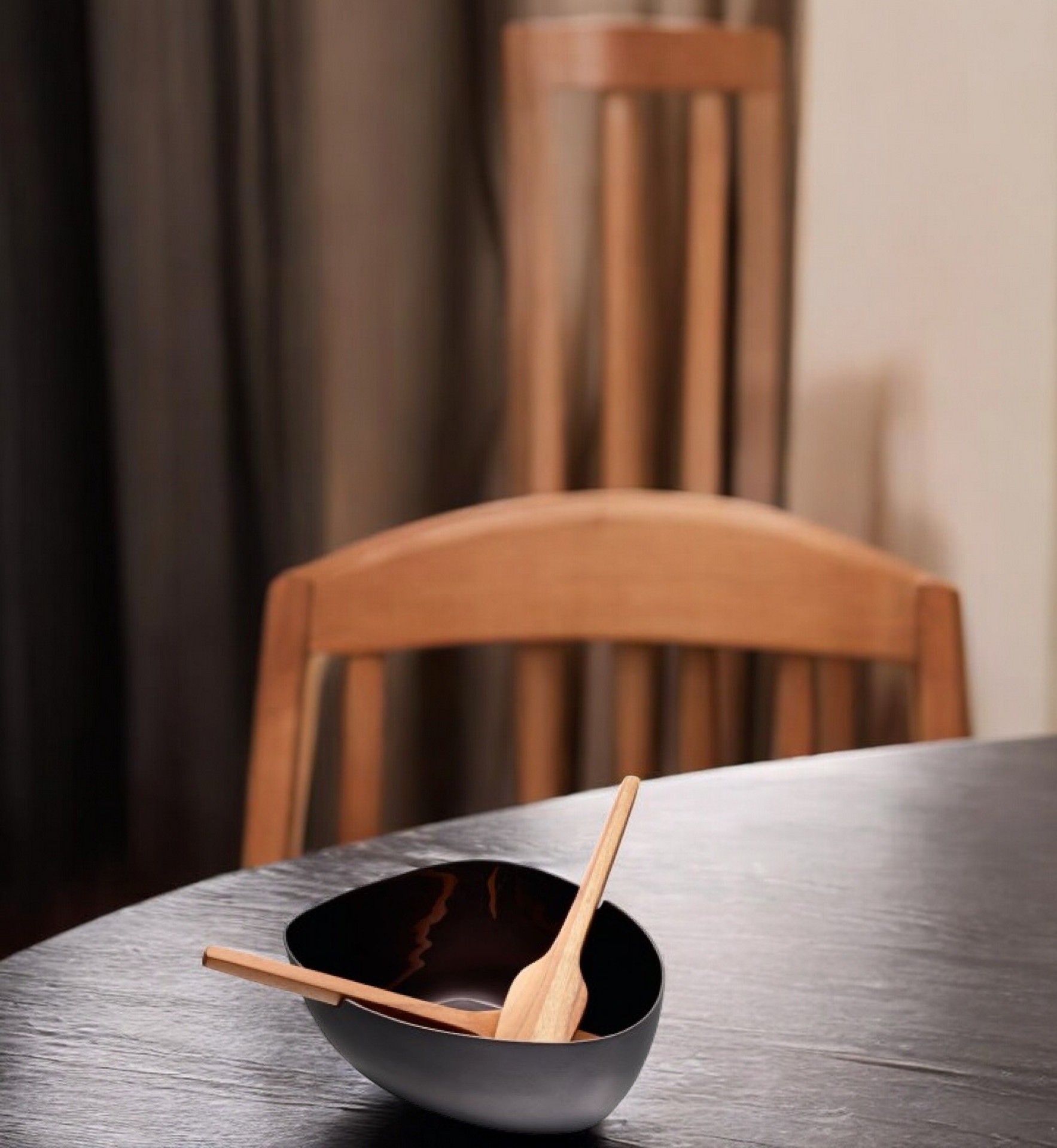 Schwarze Boat Salatschale von Philippi mit Holz Besteck auf einem dunklen Holztisch.
