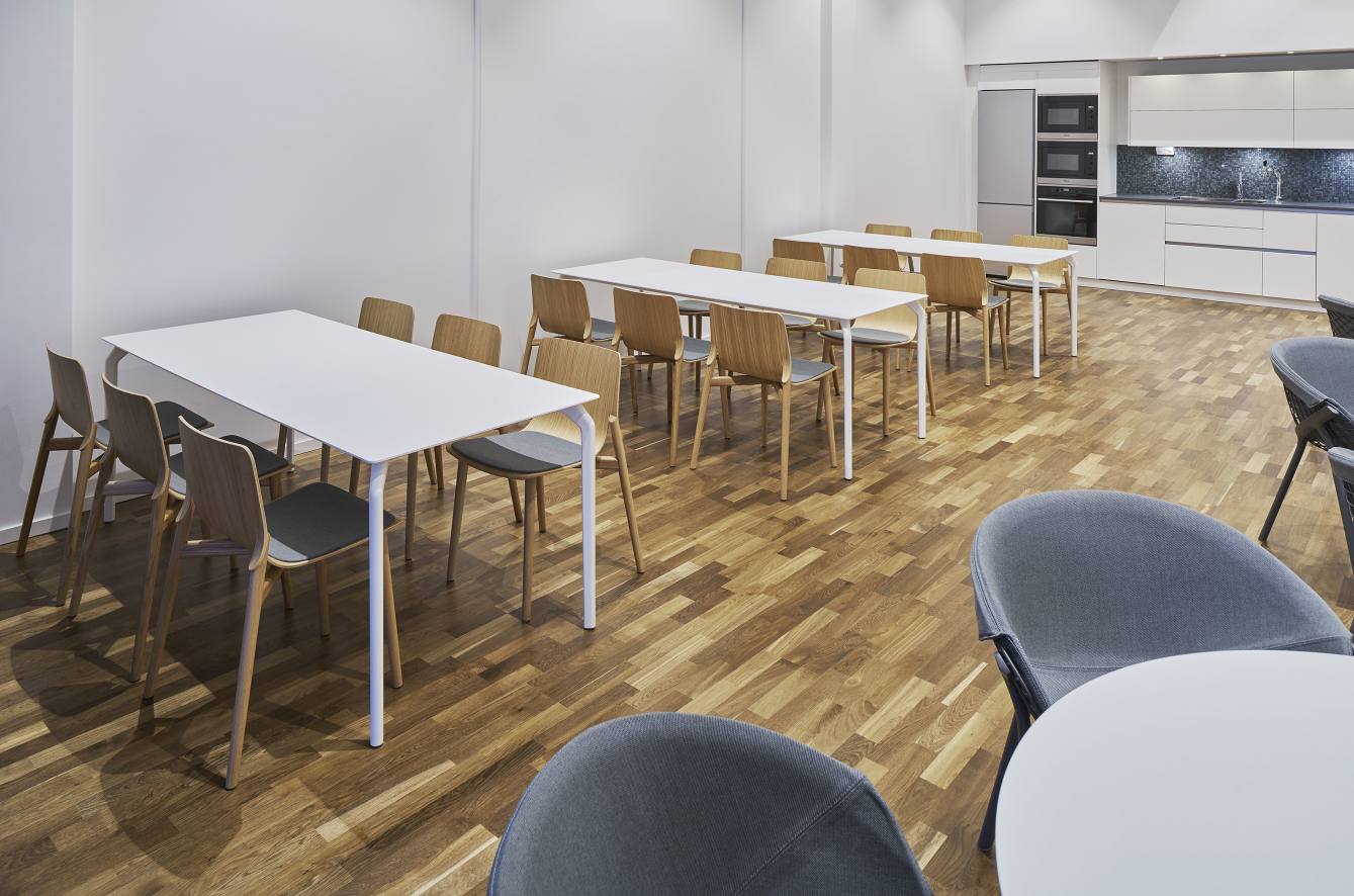 Helle Büroumgebung mit mehreren Tec Table Tischen, Holzstühlen und einer Küchenzeile im Hintergrund.