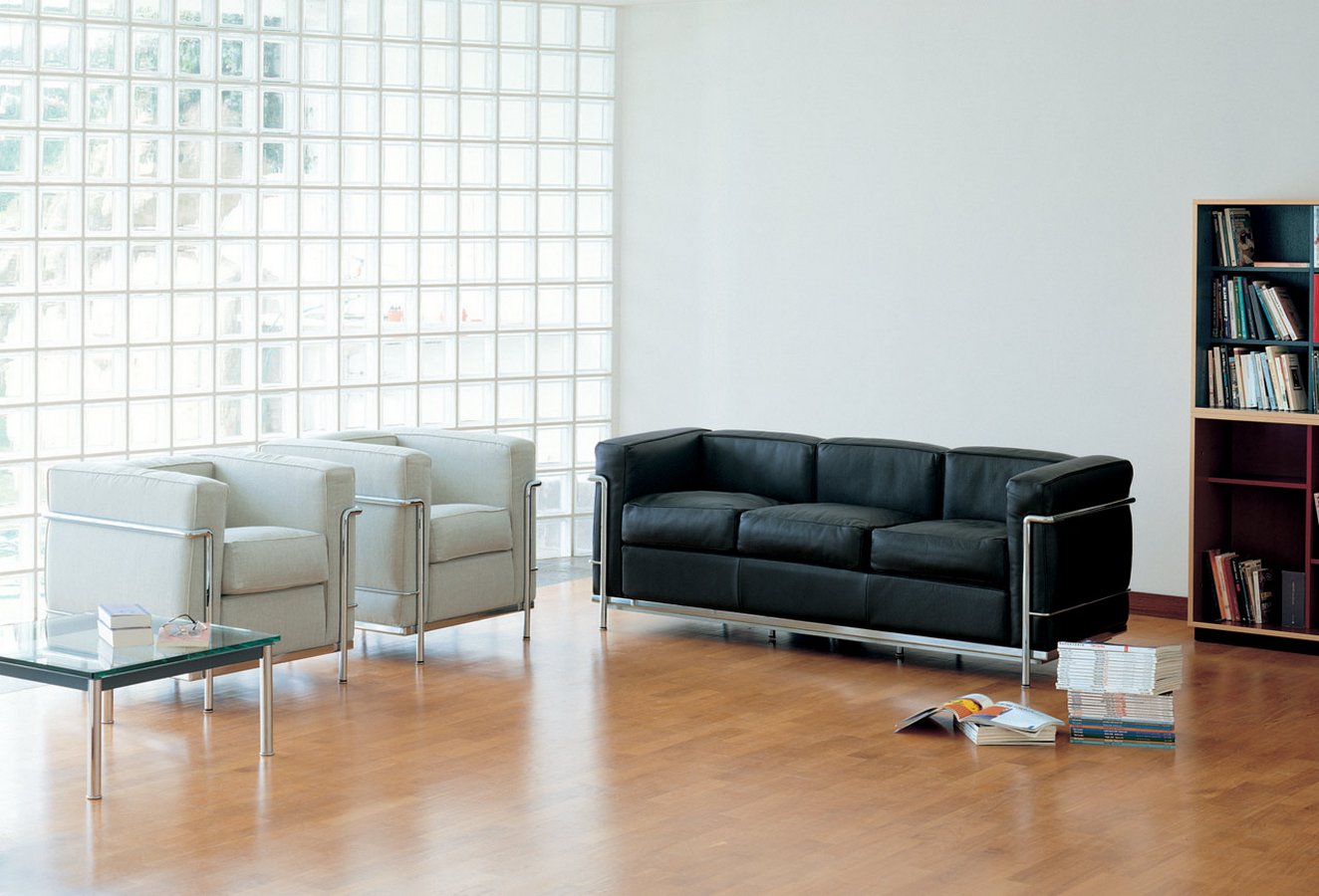 Cassina Grand Confort: Schwarzes Ledersofa und zwei helle Sessel mit Stahlrohrgestell in modernem Raum.