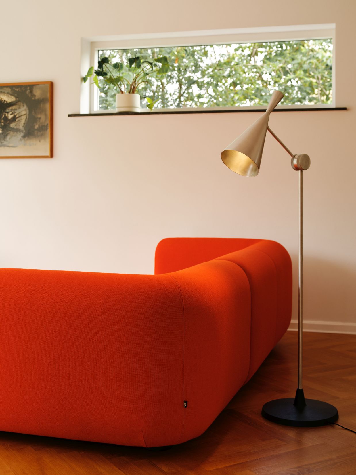 Unbeaten Stehleuchte von Tom Dixon neben einem orangefarbenen Sofa in einem hellen Wohnzimmer.