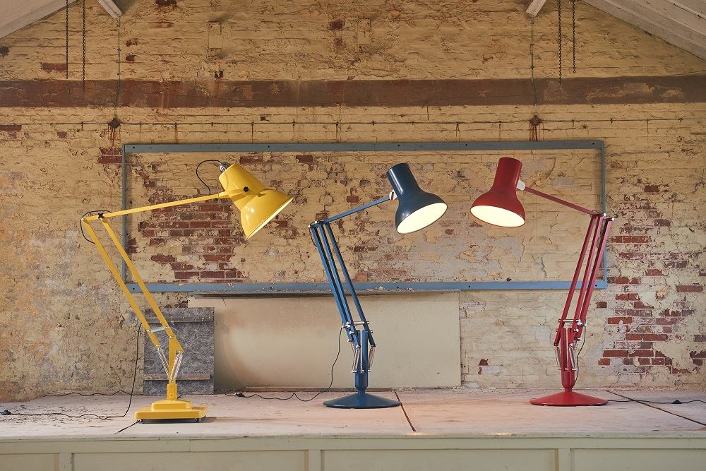 Drei farbige Anglepoise Original 1227 Giant Floor Lamp Stehleuchten vor einer Backsteinwand.