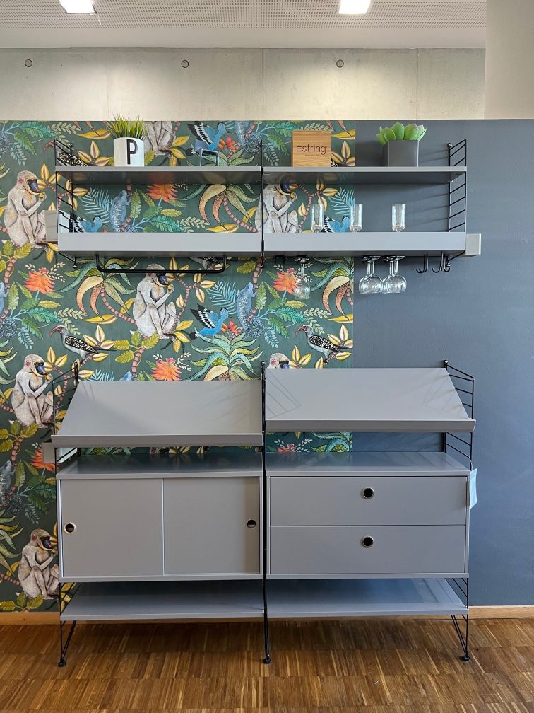 Graues String Regal mit Schränken, Regalböden und Gläserhalter vor einer Dschungeltapete. String Furniture Ausstellungstück.