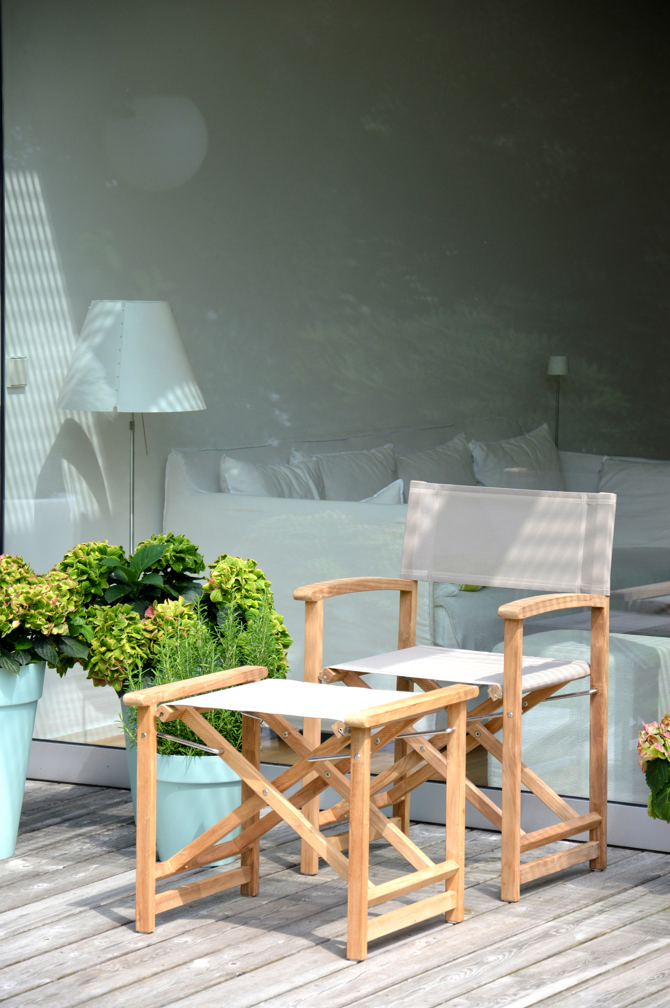 Urban Regiestuhl von Jan Kurtz mit taupefarbenem Bezug und passendem Hocker auf einer Holzterrasse.