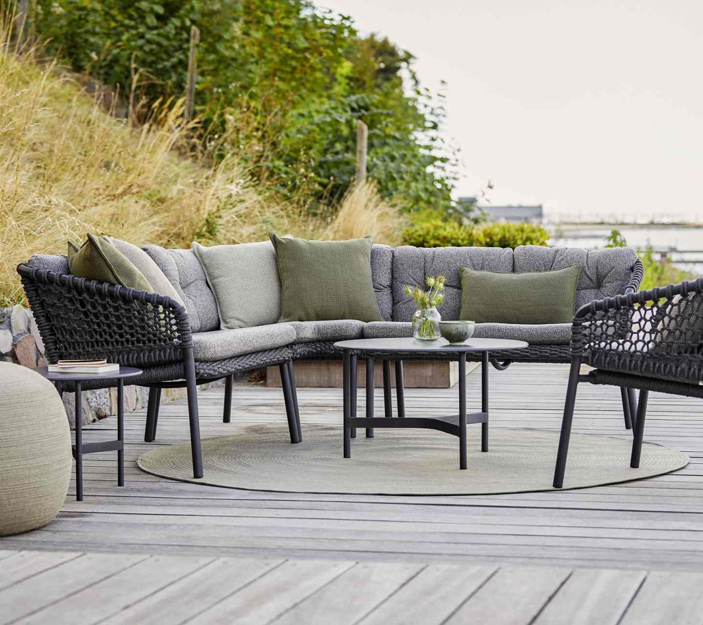 Dunkelgrauer Cane-Line Ocean Loungesessel mit Kissen und Outdoor-Möbeln auf einer Holzterrasse.