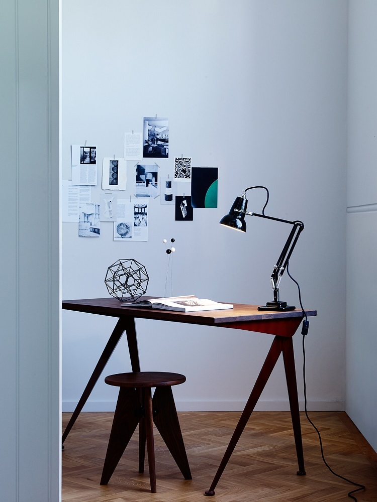Schwarze Anglepoise Original 1227 Mini Tischleuchte auf Schreibtisch mit Stuhl und Dekoration. Designklassiker für Büro und Zuhause.