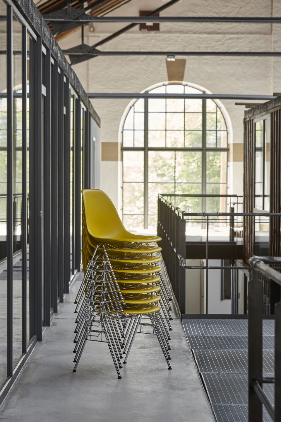 Gelbe Eames Plastic Side Chairs von Vitra, gestapelt auf einem Flur mit Fenster.