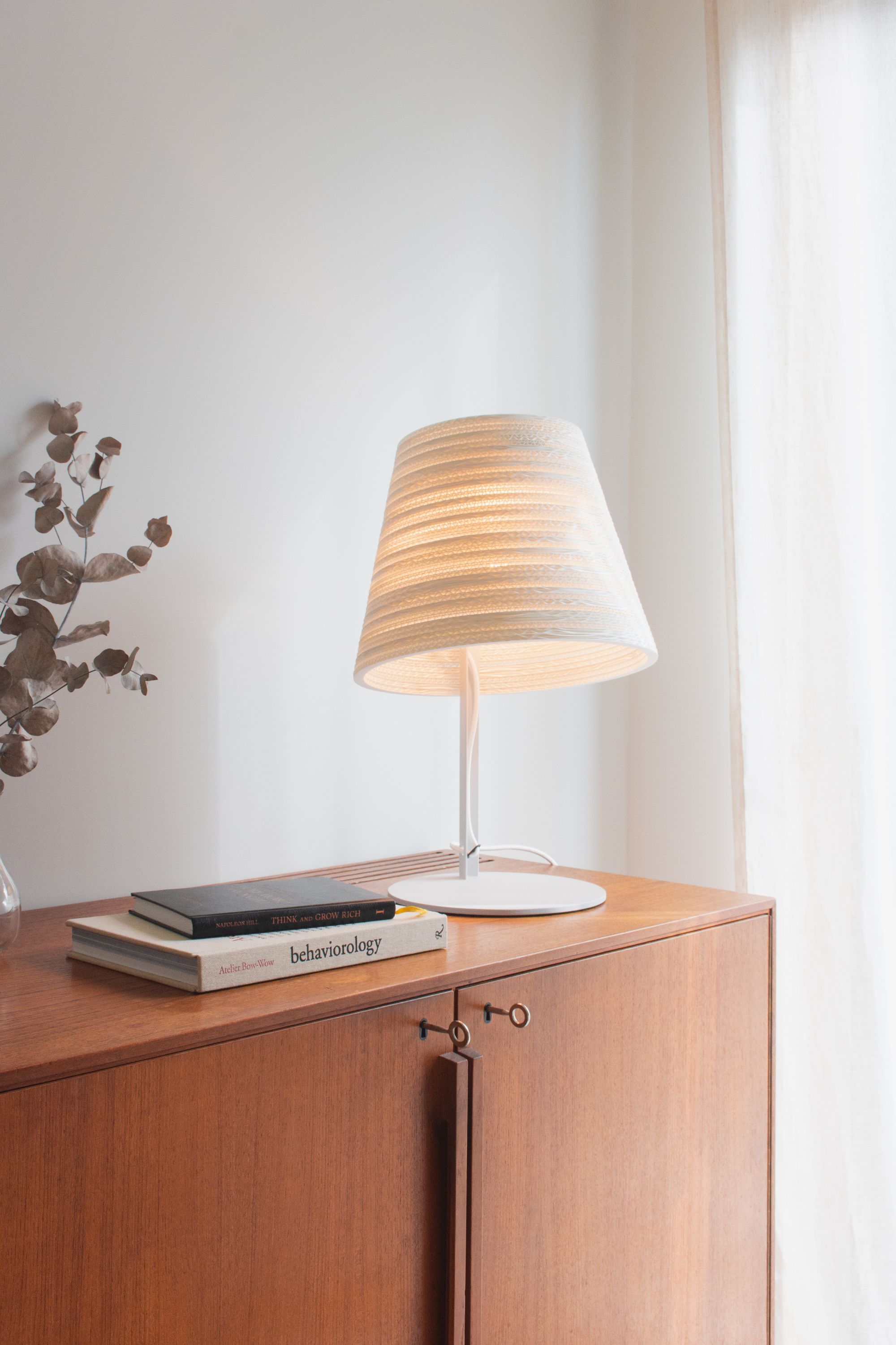 Weiße Tilt Tischlampe Scraplights von Graypants auf Holzkommode, Bücher und Trockenblumen im Hintergrund.