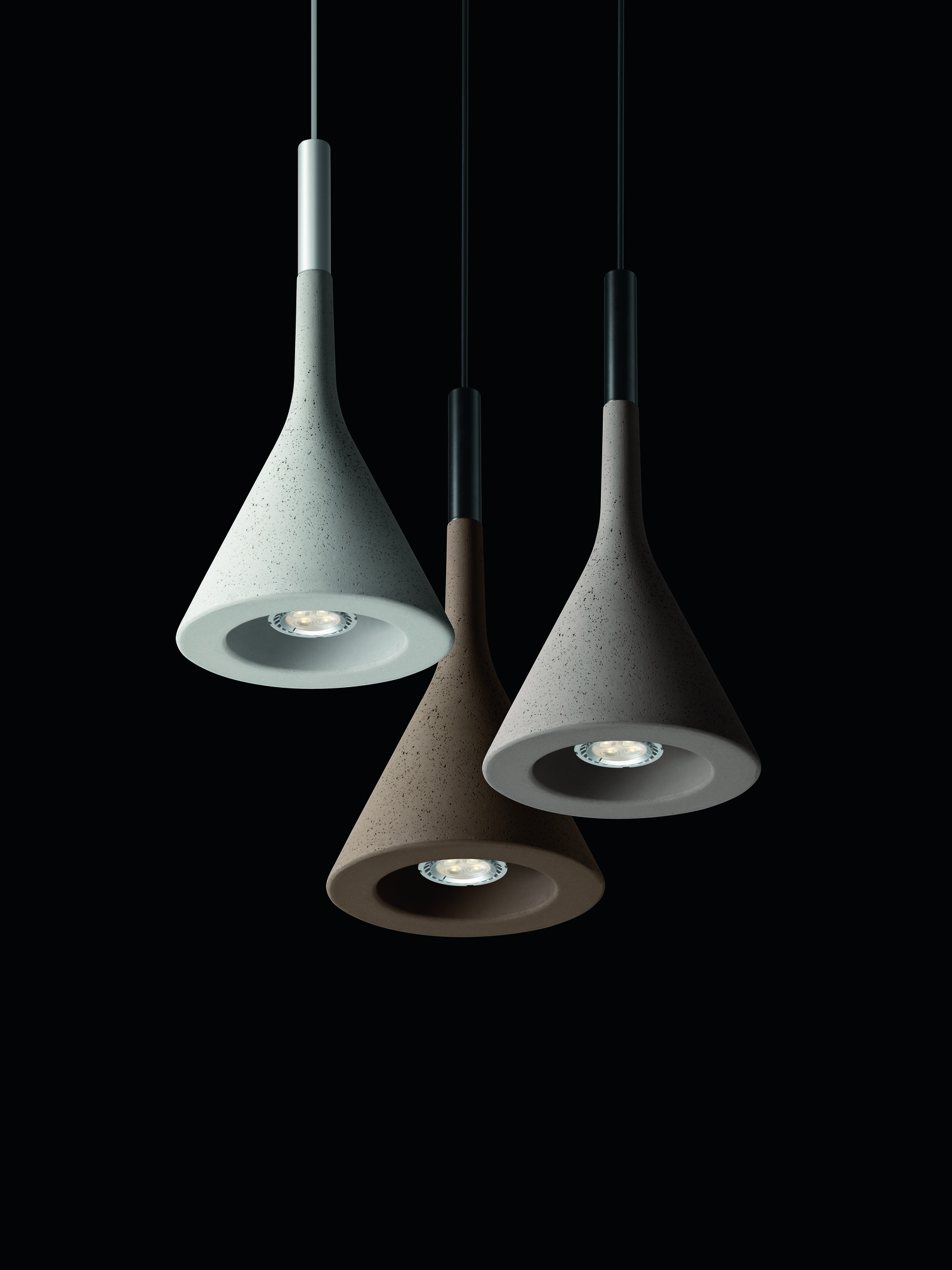 Drei Aplomb Pendelleuchten von Foscarini in Grau und Braun vor schwarzem Hintergrund.