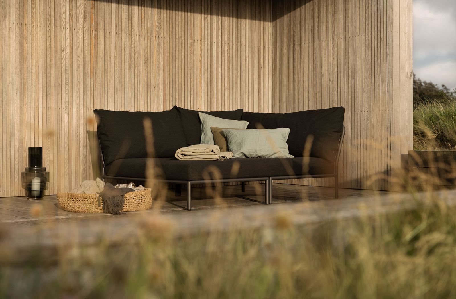 Houe Level Cozy Corner Outdoor Sofa mit Kissen und Decke auf einer Holzterrasse.