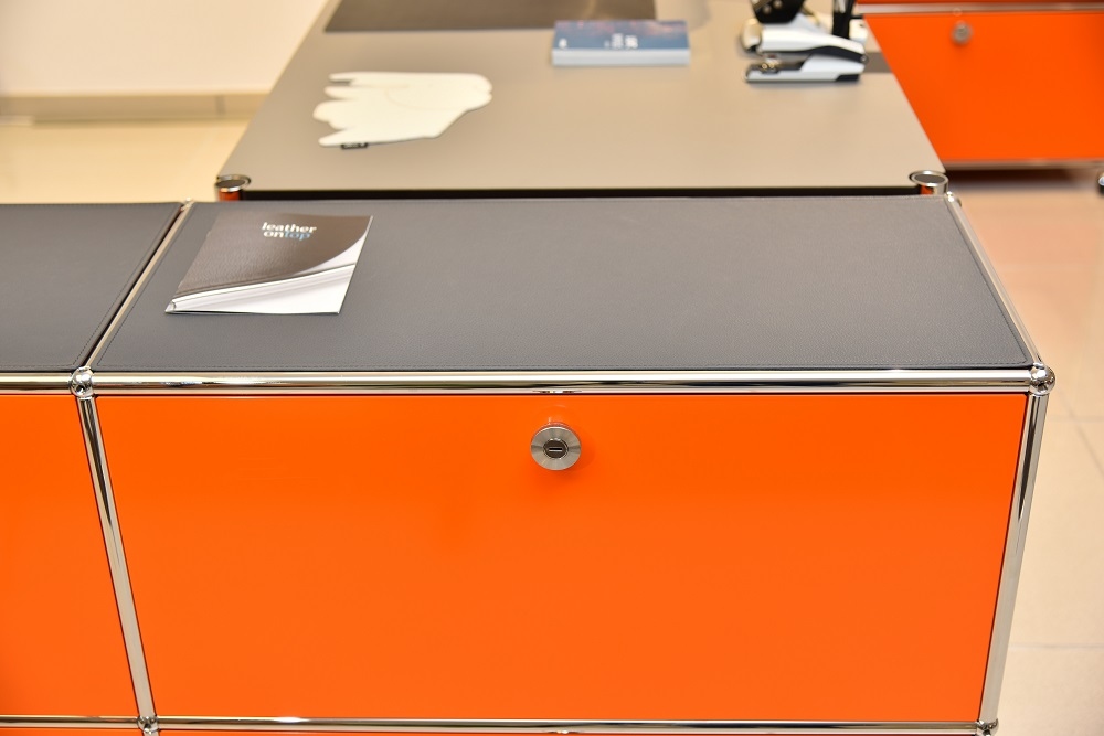 Graphitschwarze Lederauflage auf orangefarbenem USM Sideboard. Hochwertige Ledermatte als Zubehör für modulare Möbel.