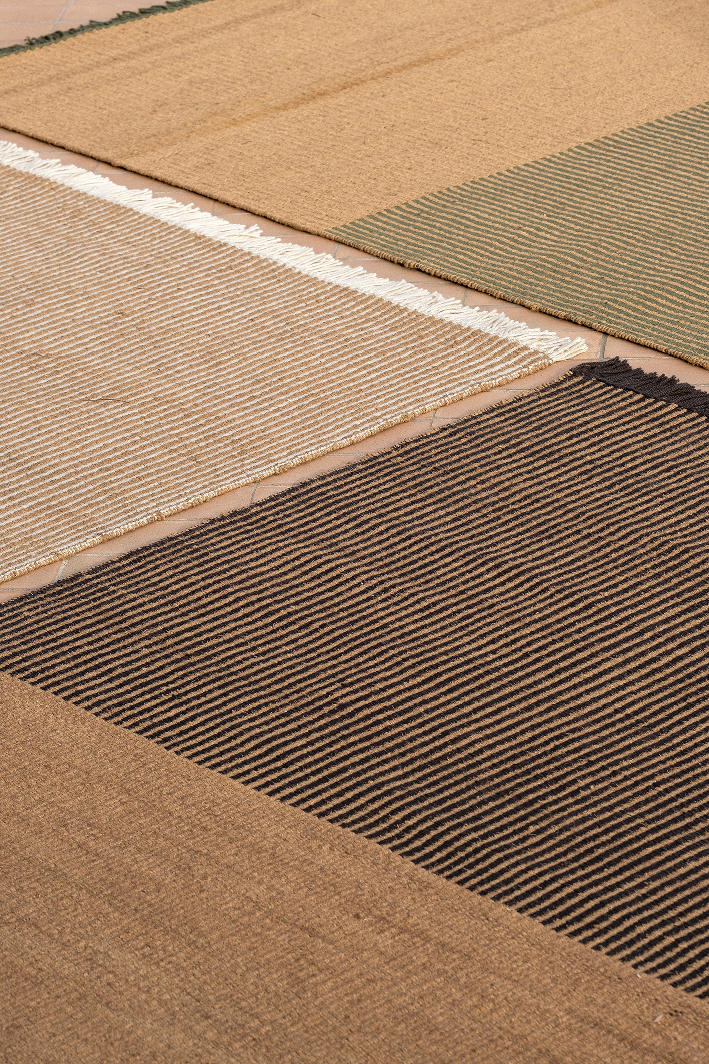 Detailaufnahme von mehreren Outdoor Teppichen, darunter ein schwarzer Nanimarquina Teppich mit Streifenmuster.