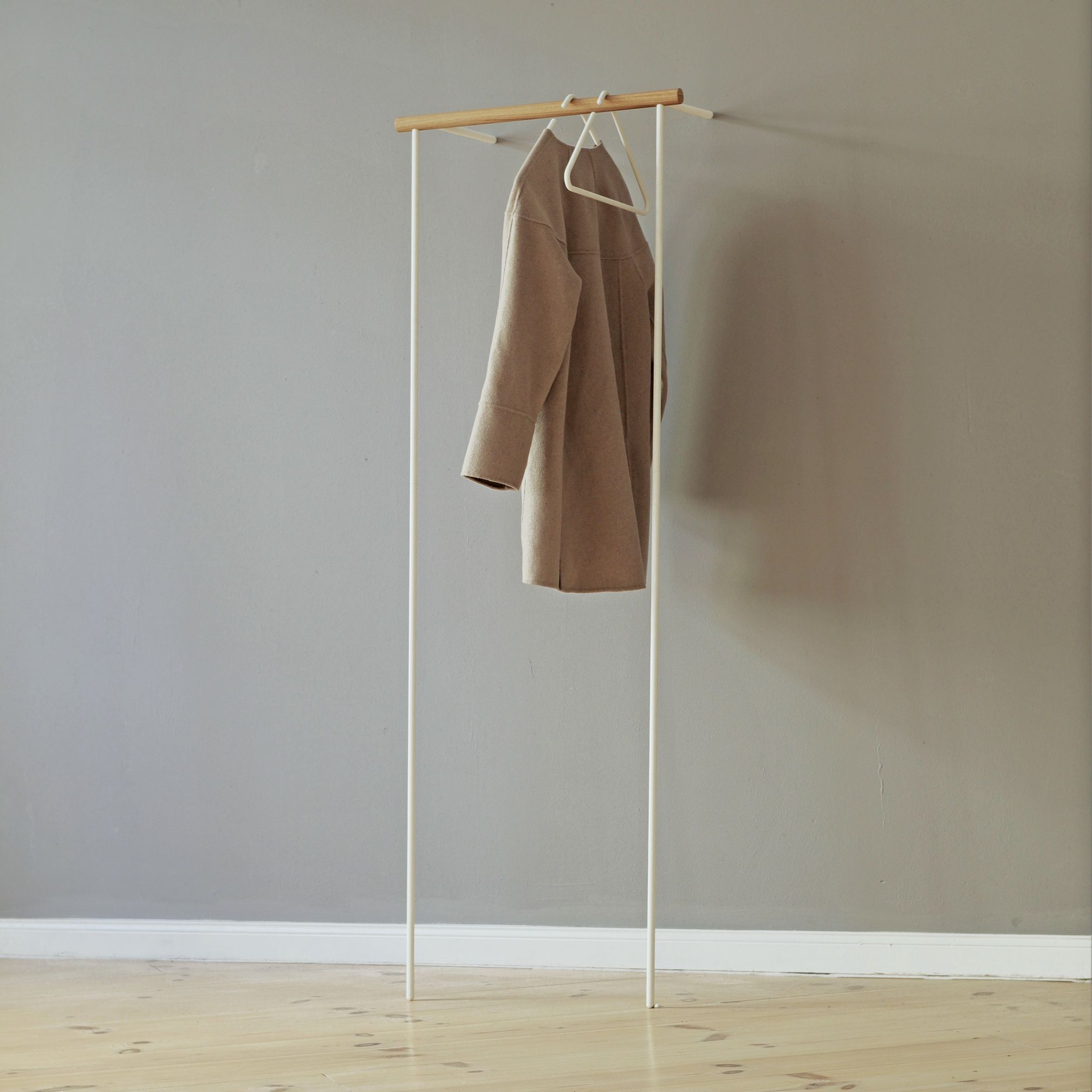 Weiße Leanon II Anlehngarderobe von Roomsafari mit Mantel an der Wand. Moderne Garderobenlösung.