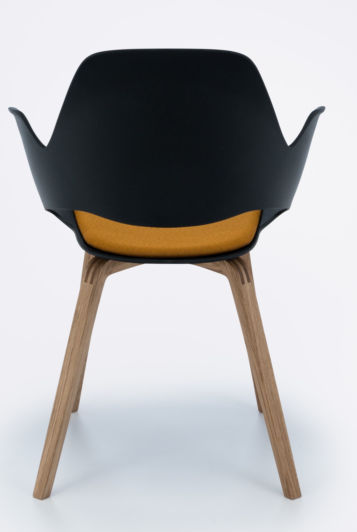 Rückansicht des Falk Stuhls von Houe: Schwarze Sitzschale, gelbe Polsterung und Eichenholzbeine.