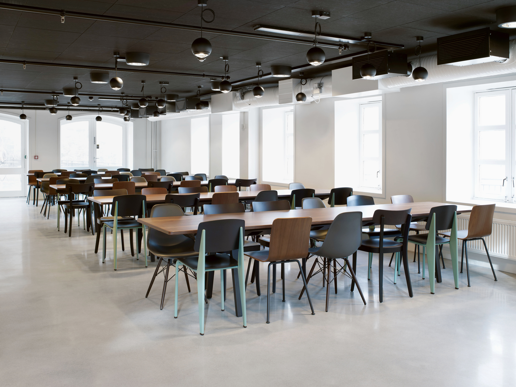 Innenaufnahme: Viele Vitra Hal Ply Stühle in verschiedenen Farben an Holztischen.