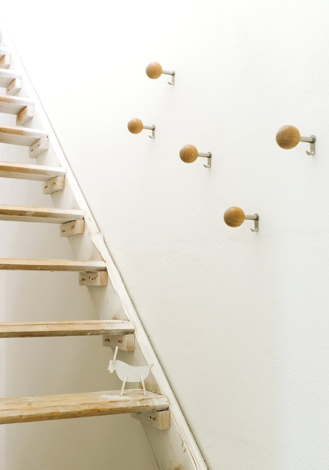 Dots Wandhaken aus Nussbaumholz an weißer Wand neben Treppe. Design Garderobenhaken für Flur.