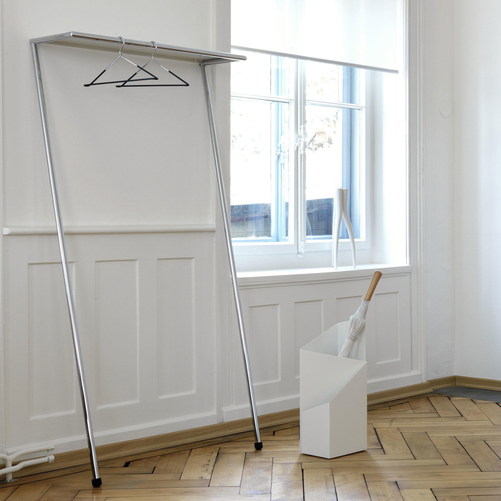 Zen Anlehngarderobe Mox in Chrom Glanz vor weißer Wand mit Kleiderbügeln und Schirmständer.