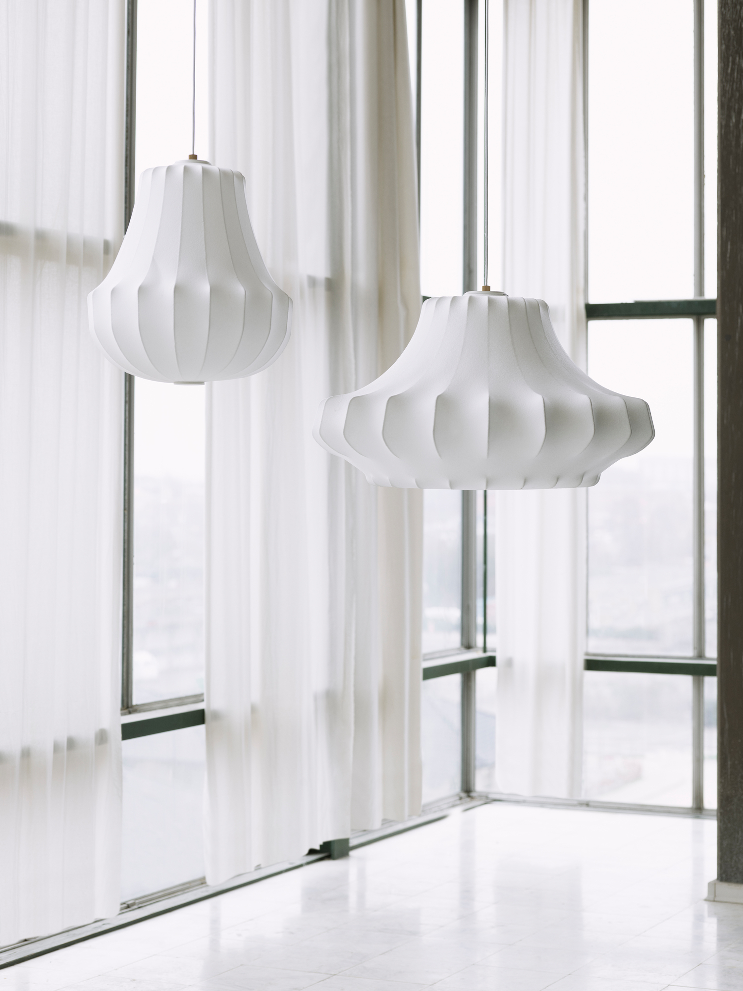 Zwei große, weiße Phantom Lamp Pendelleuchten von Normann Copenhagen vor einem Fenster.
