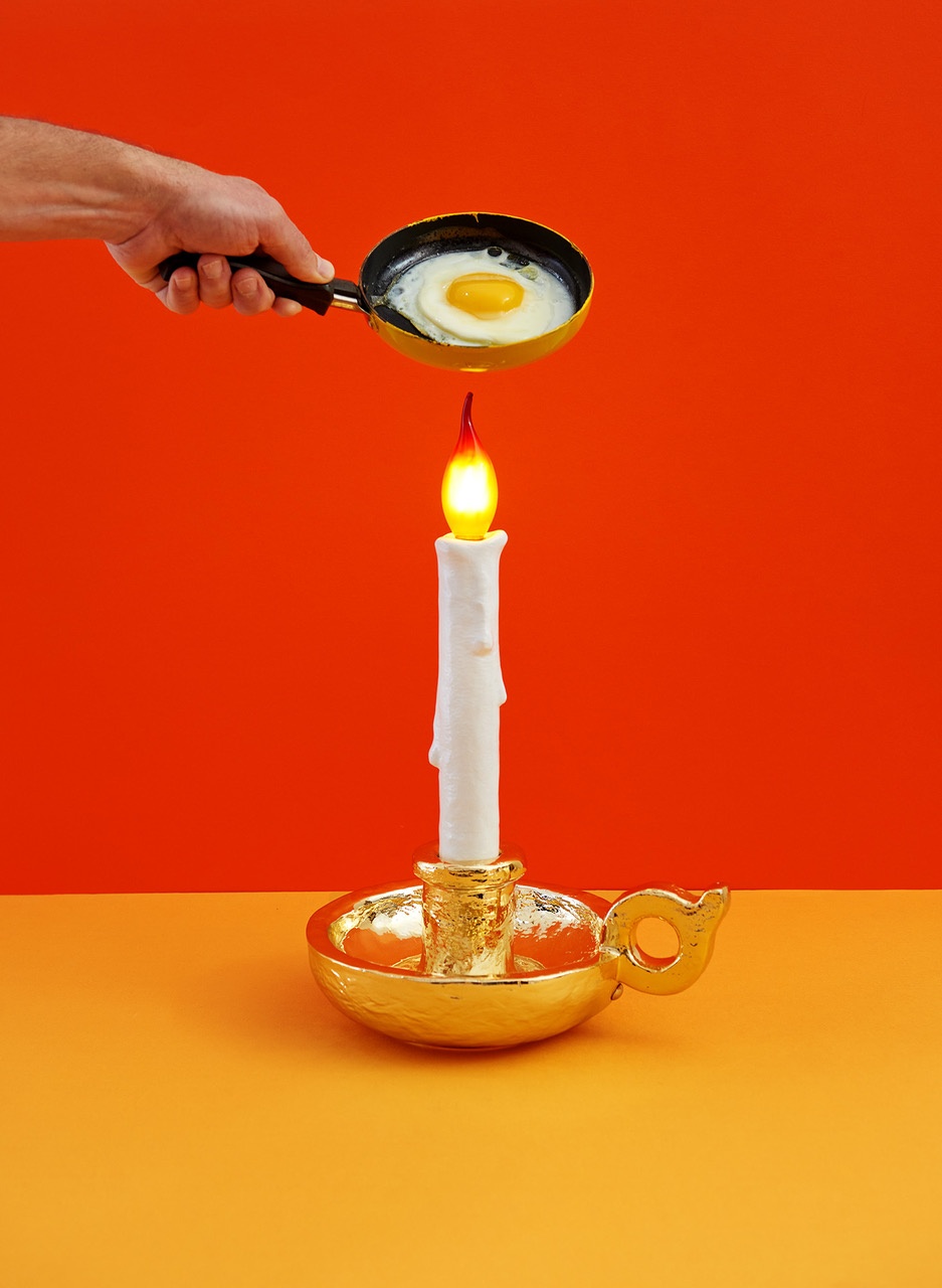 Grimm Lamp Akkuleuchte: Weißes LED-Kerzenlicht in goldenem Kerzenständer, darüber eine Bratpfanne mit Spiegelei.