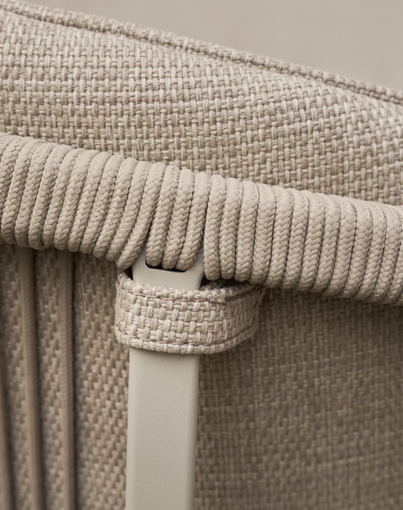 Detailaufnahme: Lagrasse Stuhl mit beigem Sitzkissen und geflochtenen Armlehnen für den Outdoor-Bereich.