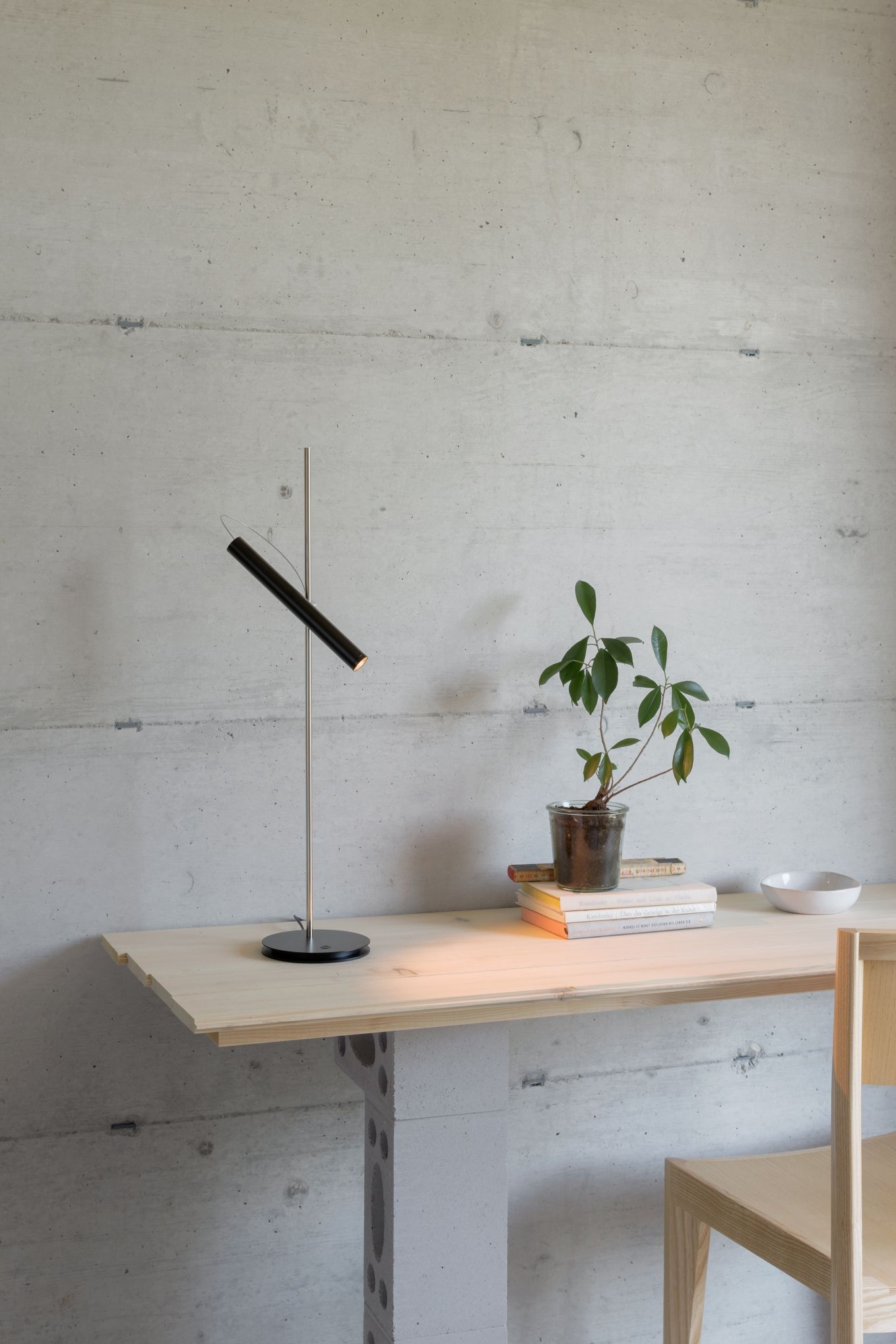 LINIjA T Tischleuchte von Baltensweiler auf einem Holztisch, daneben Bücher und eine Pflanze.