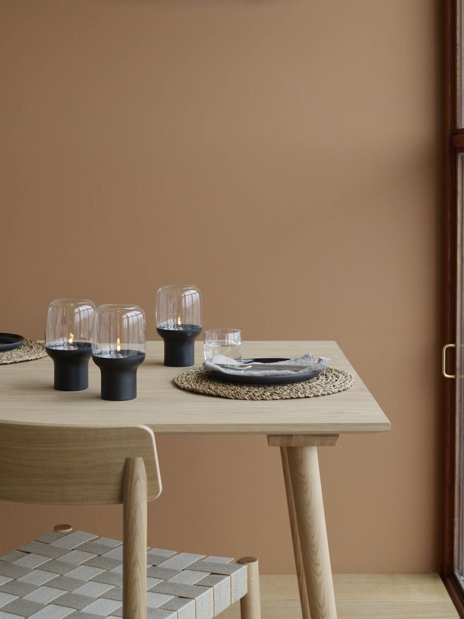 Tischdekoration mit Stelton Hoop Hurricane Windlichtern, Glas, Geschirr und Stuhl im minimalistischen Design.