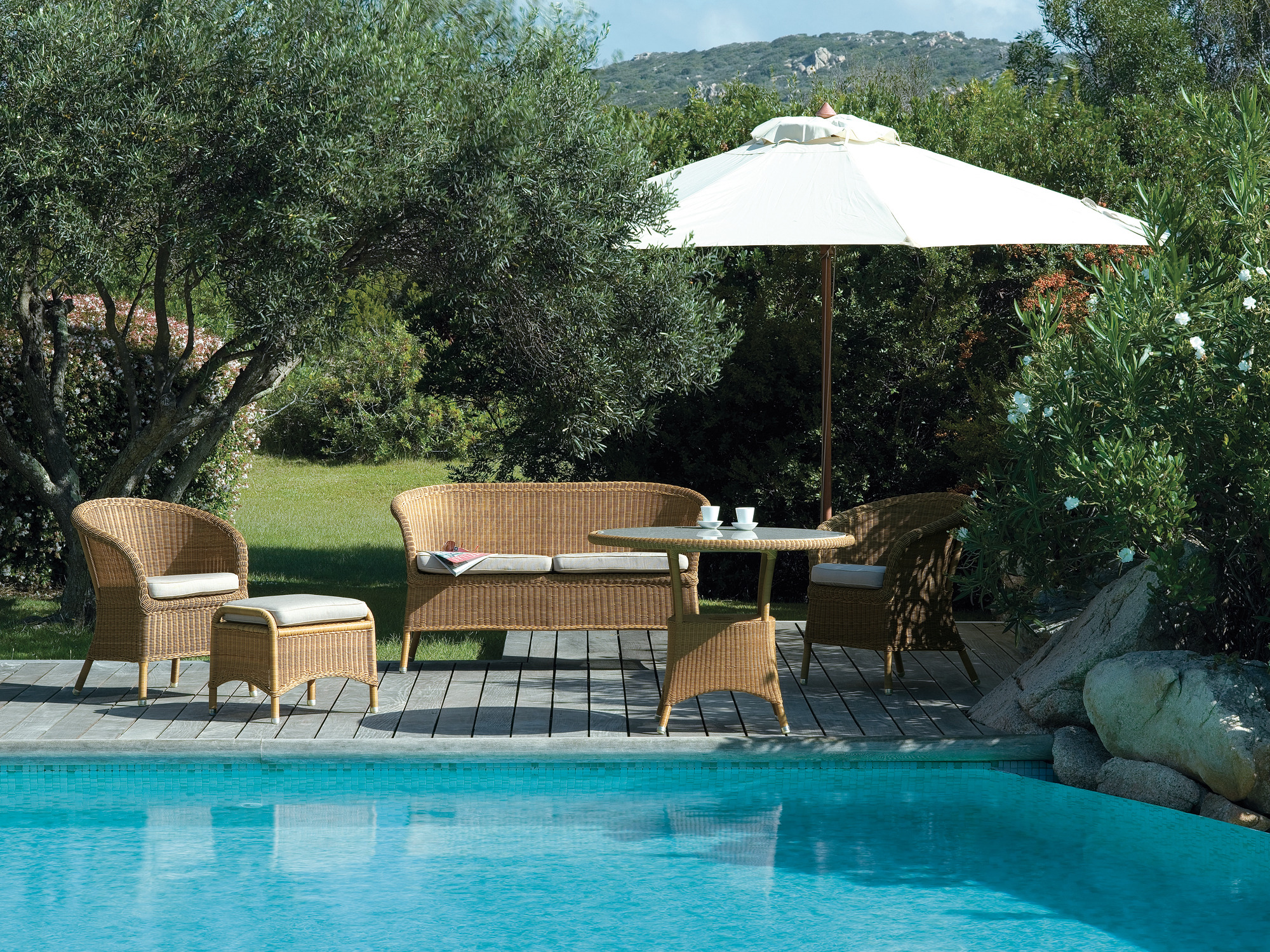 Derby Outdoor Sessel Cane-Line aus Rattan mit Sofa, Tisch und Sonnenschirm am Pool.