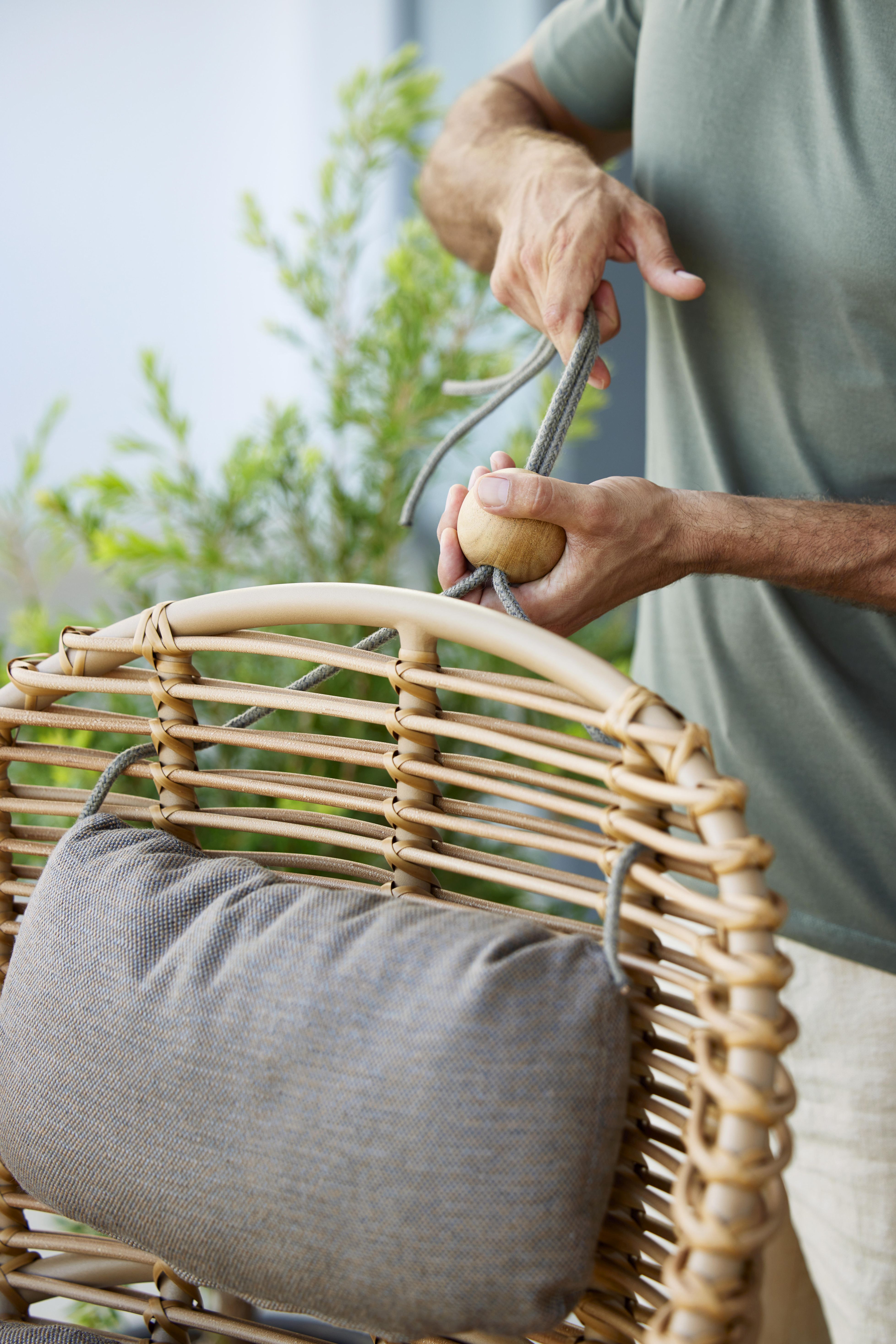 Mann befestigt Kissen am Cane-Line Hive Sessel aus Rattan mit Teakholz-Details.