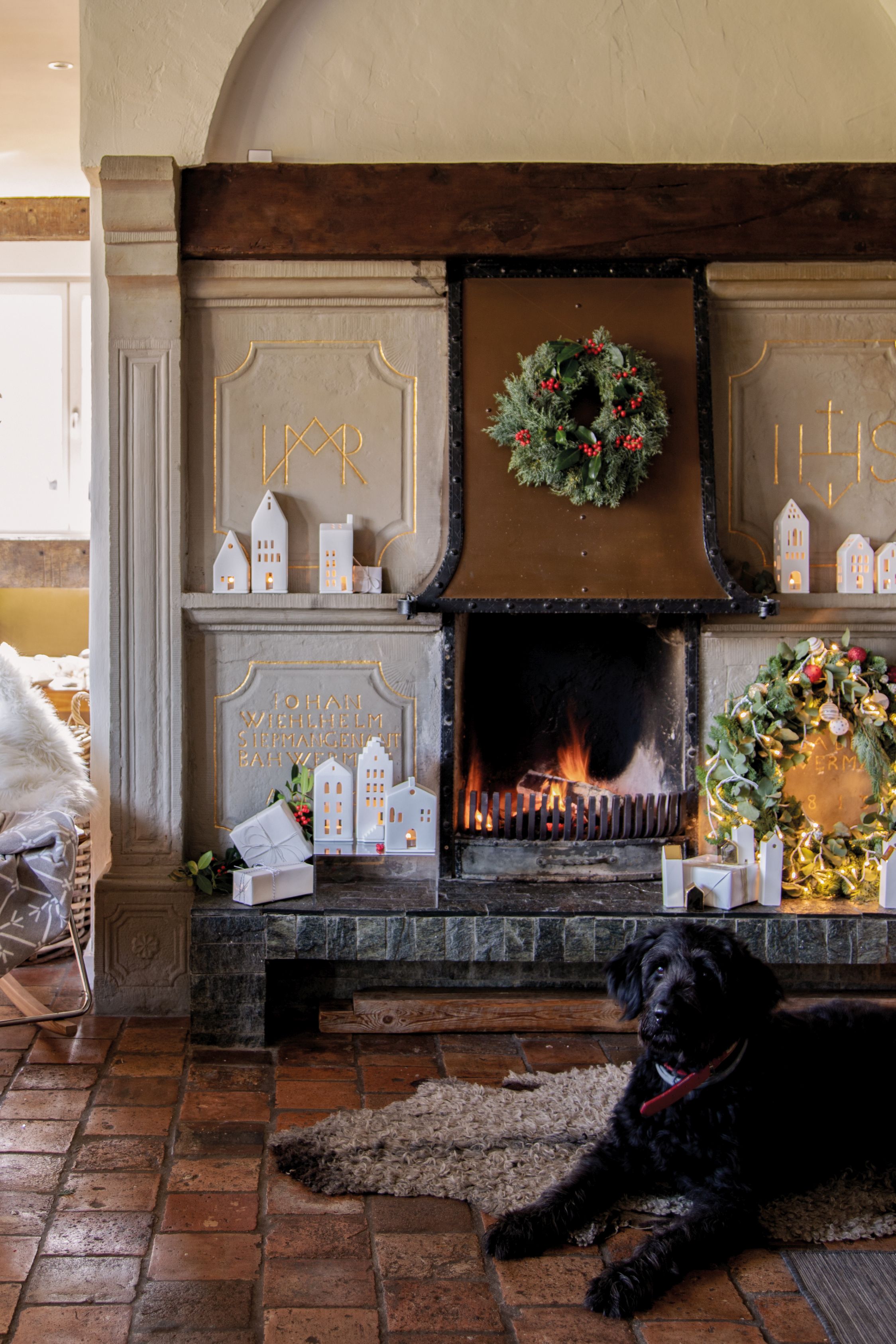 Großes Lichthaus Giebeldach als festliche Dekoration am Kamin mit Kränzen und einem Hund.