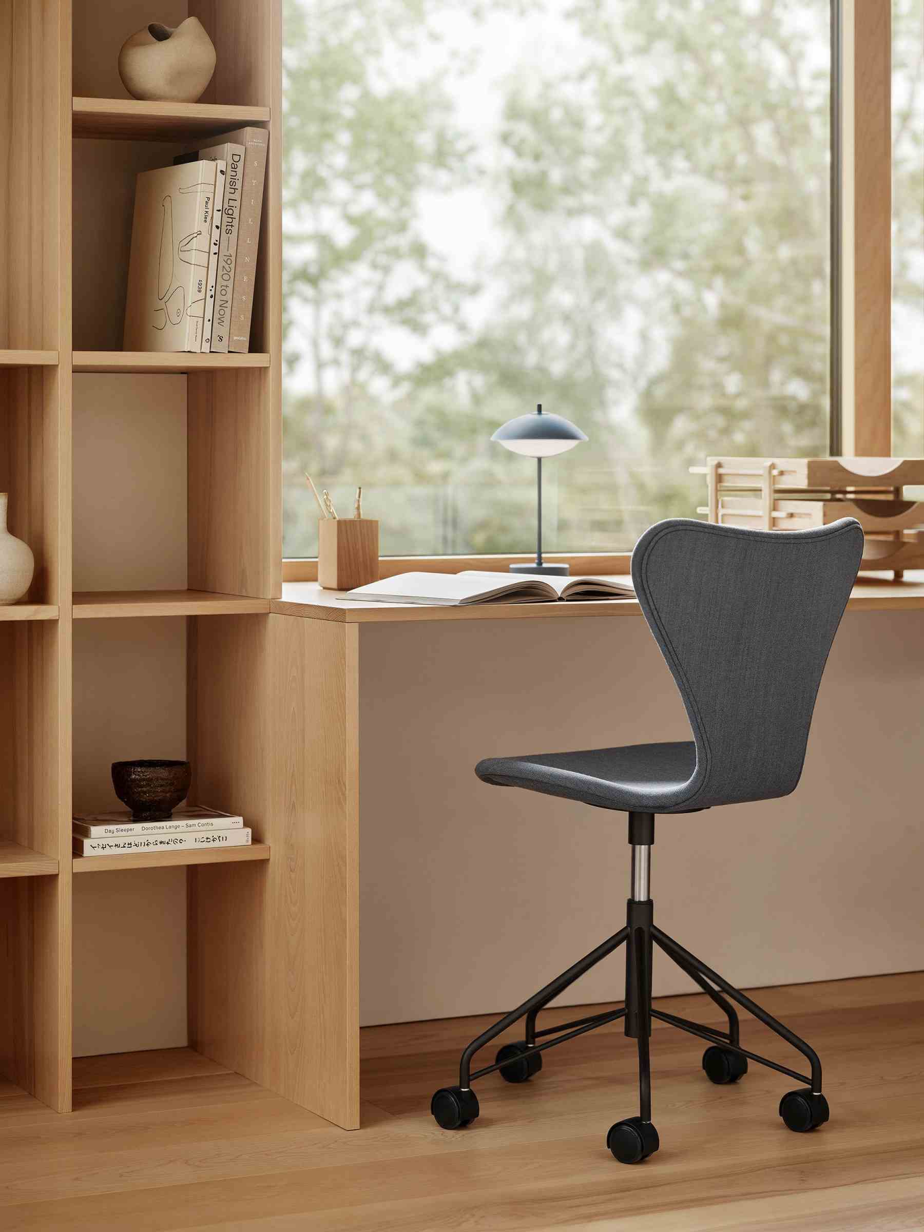 Schreibtisch mit Fritz Hansen Clam Tischleuchte und Bürostuhl vor Fenster, minimalistisches Design.