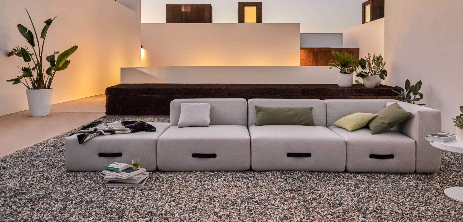 Graue modulare Couch mit Kissen und Decke auf Kiesboden. Modernes Sofa für Wohnzimmer und Lounge.