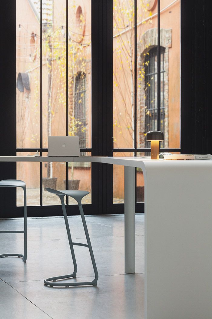 Moderner Arbeitsplatz mit minimalistischem Schreibtisch, grauen Barhockern und stilvoller Tischleuchte für Büro oder Homeoffice.