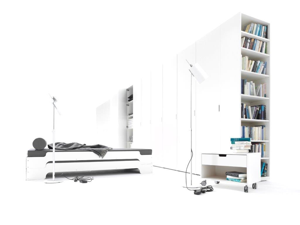 Weißer Müller Möbelwerkstätten Nachttisch mit Schublade und Rollen neben Bücherregal und Stapelliege.