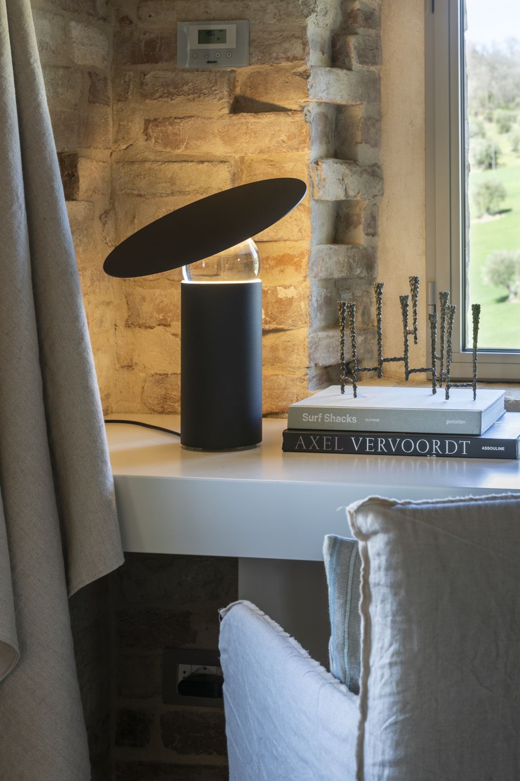 Moderne schwarze Tischleuchte mit rundem Lampenschirm auf einem Schreibtisch, neben Büchern und Dekoration.